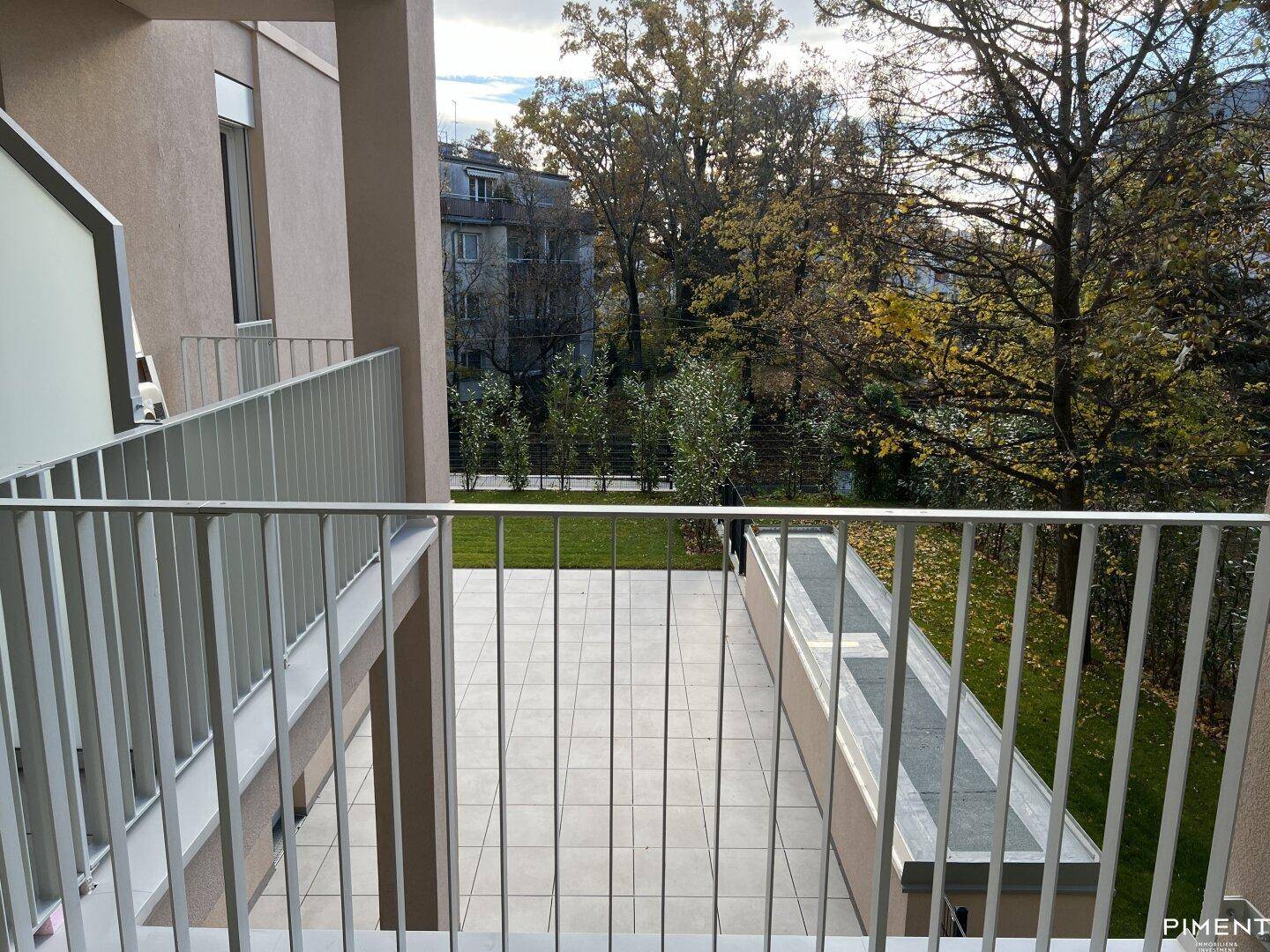 Balkon mit Fliesenboden und Blick auf einen gepflegten Gartenbereich mit Rasen und Bäumen.