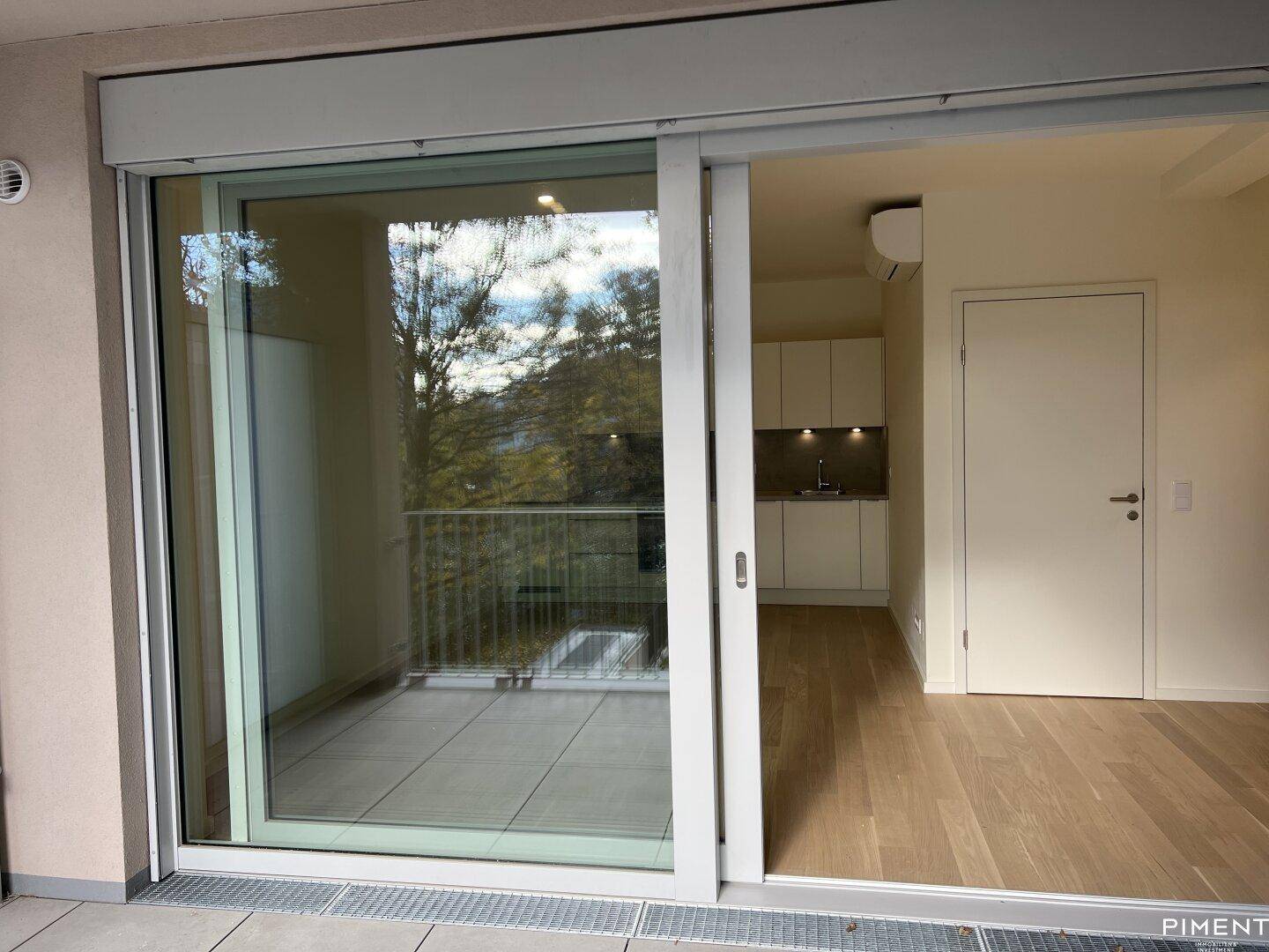 Blick vom Balkon in den hellen Wohnbereich mit Küchenzeile und Parkettboden.