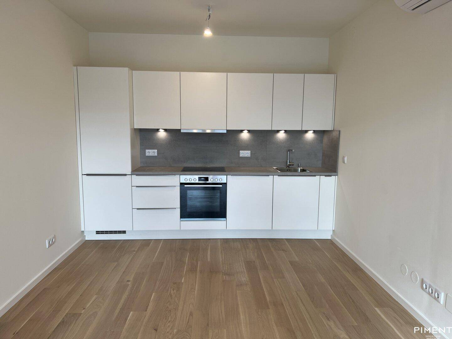 Moderne Einbauküche mit weißen Fronten, integrierten Geräten und dunkler Arbeitsplatte.