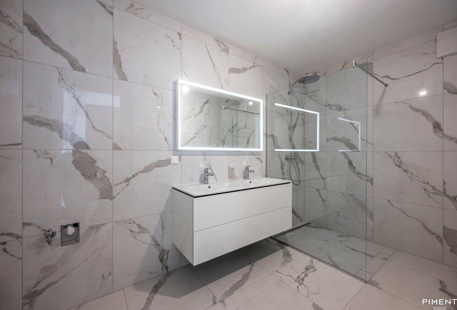 Elegantes Badezimmer mit großformatigen Marmorfliesen, Doppelwaschbecken und einer geräumigen begehbaren Dusche.