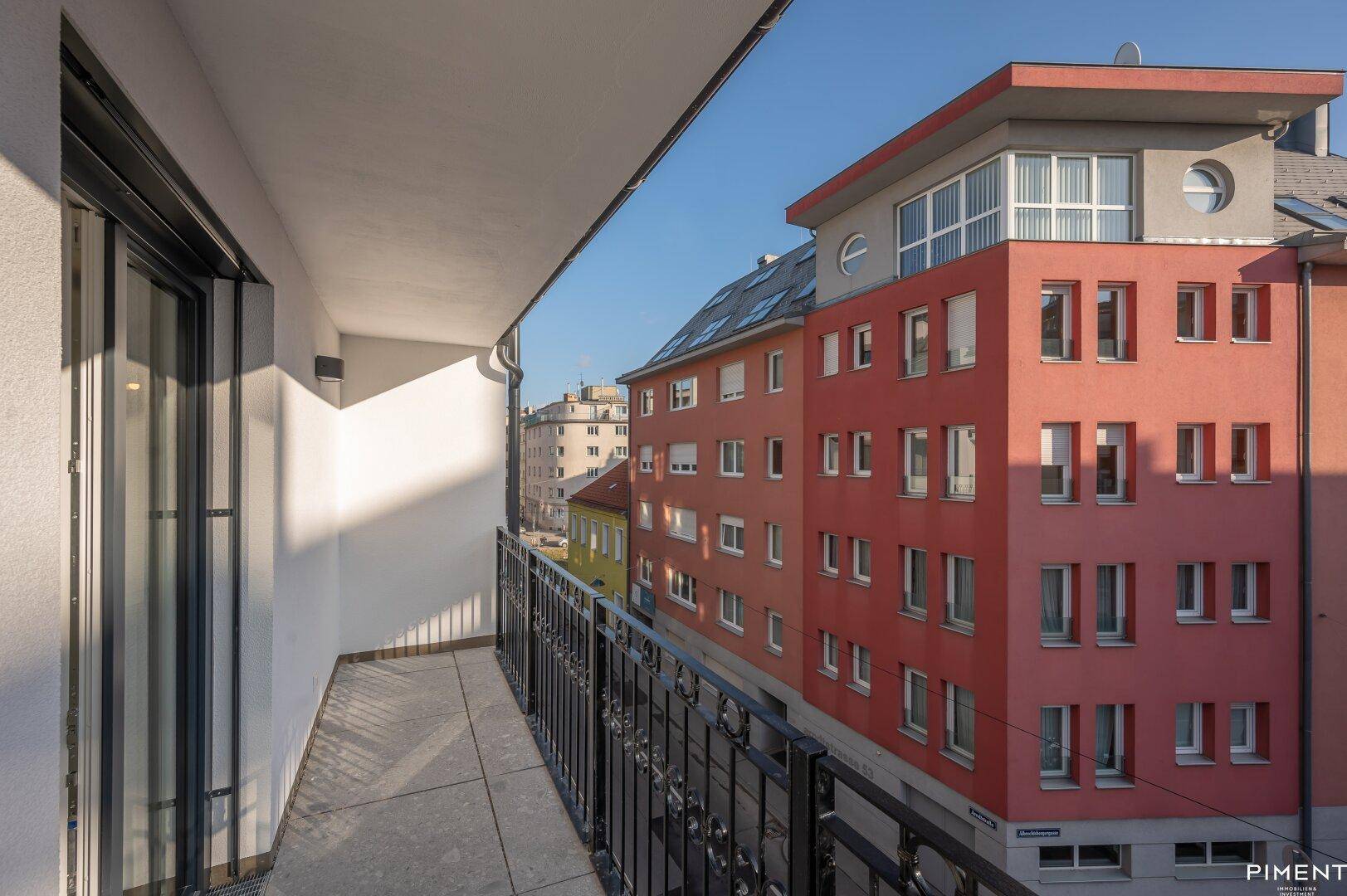 Balkon mit Fliesenboden und schmiedeeisernem Geländer bietet Blick auf die umliegenden Gebäude und die Straße.
