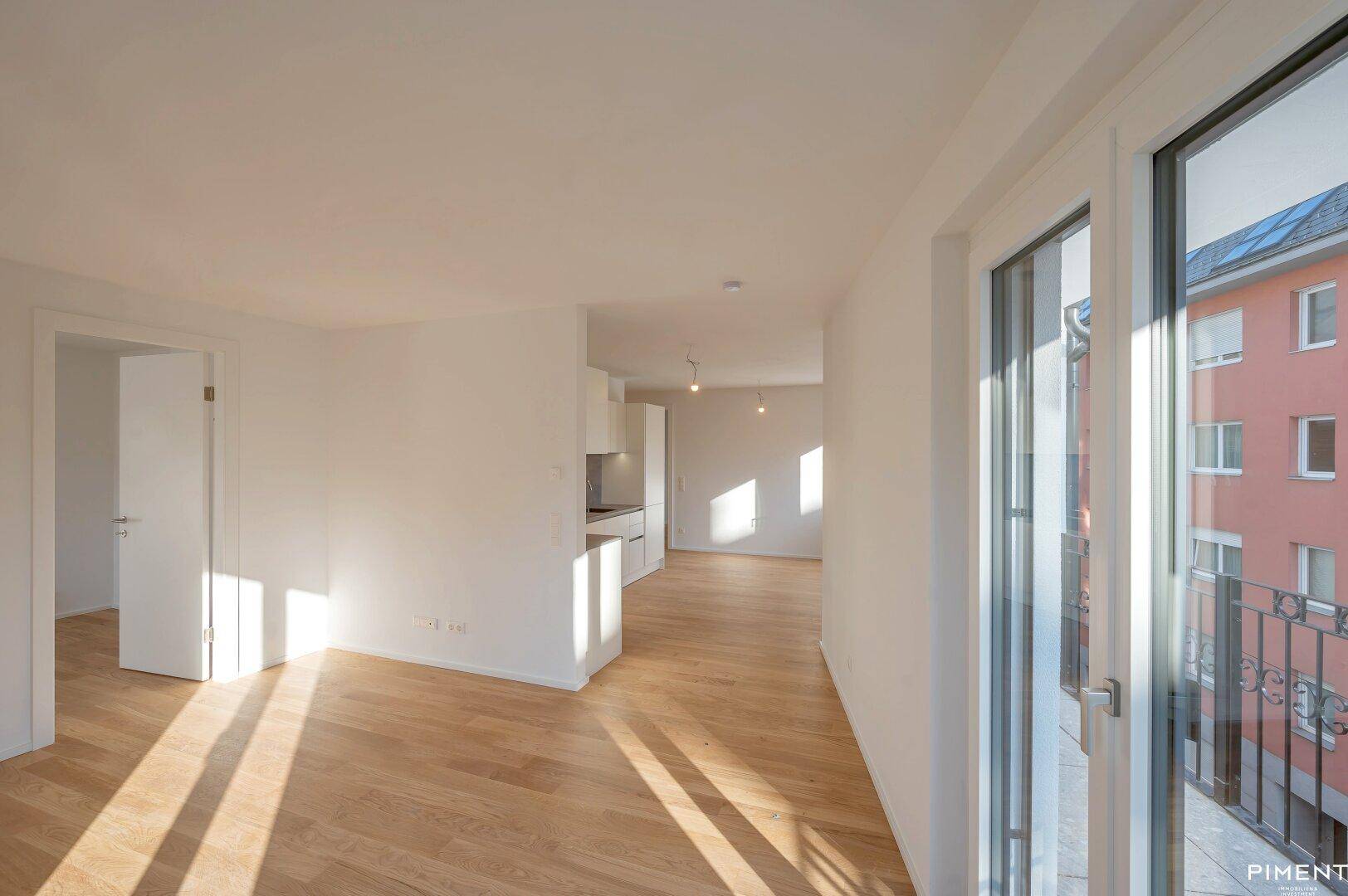Heller offener Wohnbereich mit Holzboden und Zugang zu einem Balkon, durchflutet von natürlichem Sonnenlicht.