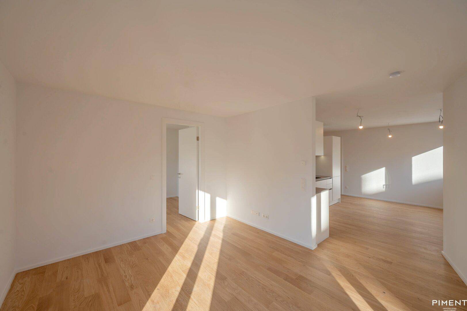 Lichtdurchfluteter offener Wohnbereich mit hellem Parkettboden und weißen Wänden, ideal für modernes Wohnen.
