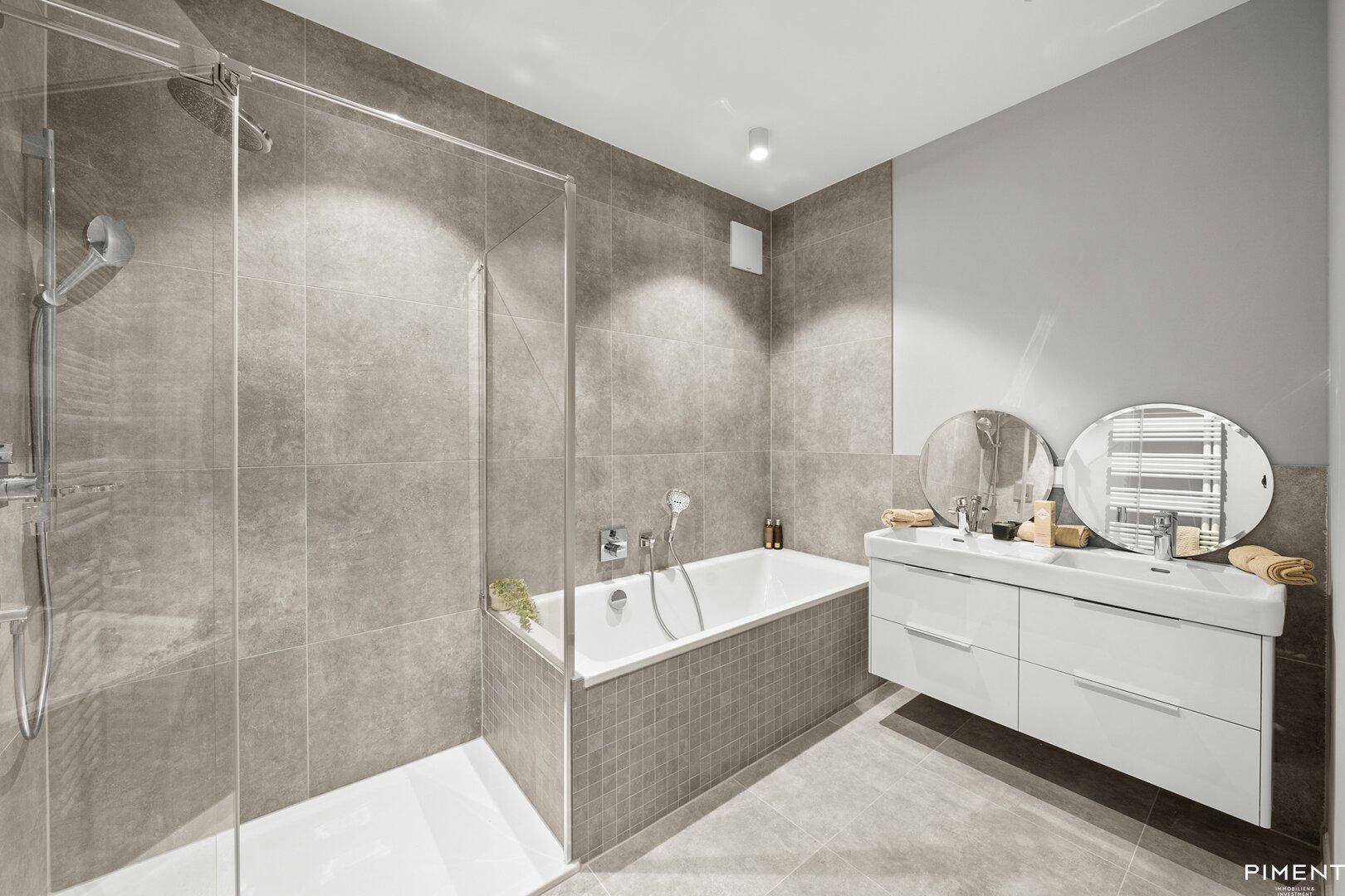 Modernes Badezimmer mit großen grauen Fliesen, einer Badewanne, einer begehbaren Dusche und einem Doppelwaschbecken.