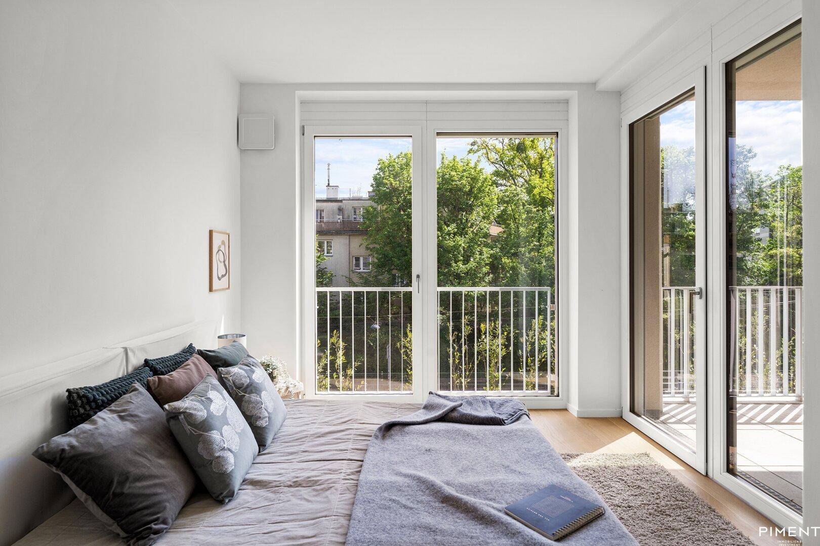 Schlafzimmer mit großem Fenster, das viel Tageslicht hereinlässt und einen grünen Ausblick bietet.