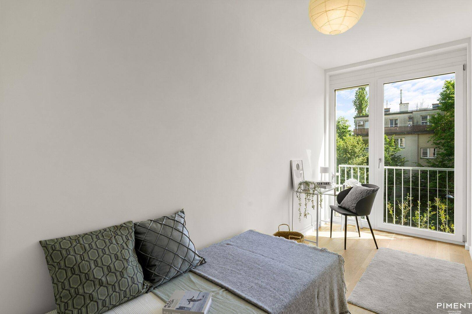 Helles Schlafzimmer mit Schreibtisch, Holzboden und großem Fenster mit Blick ins Grüne.