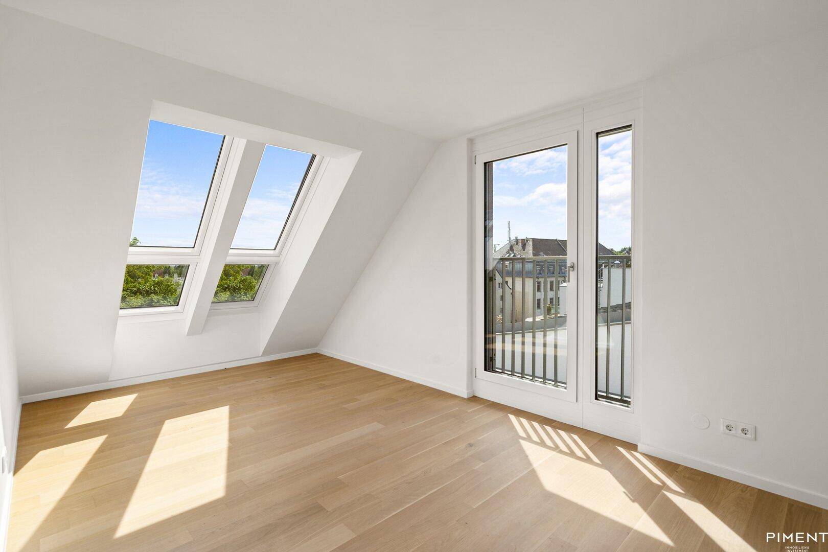 Helles Dachzimmer mit Holzboden, Dachfenstern und Zugang zu einem französischen Balkon.