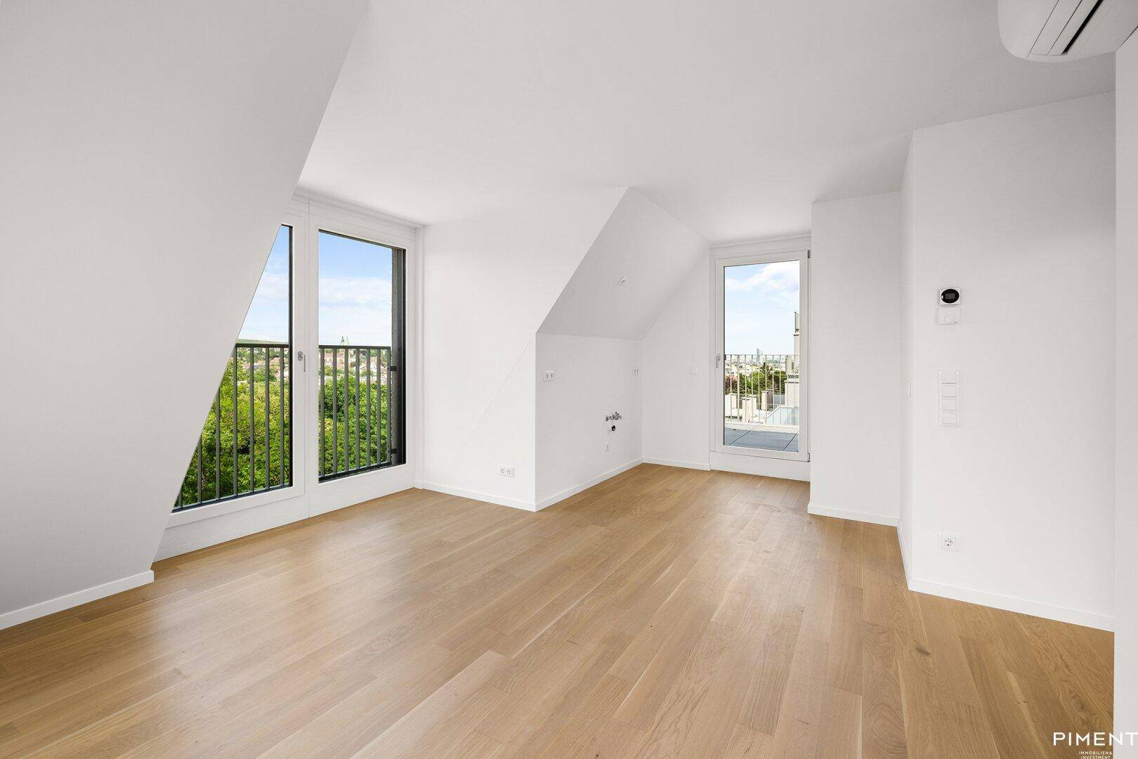 Geräumiges Dachzimmer mit Holzboden, mehreren Fenstern und Klimaanlage.