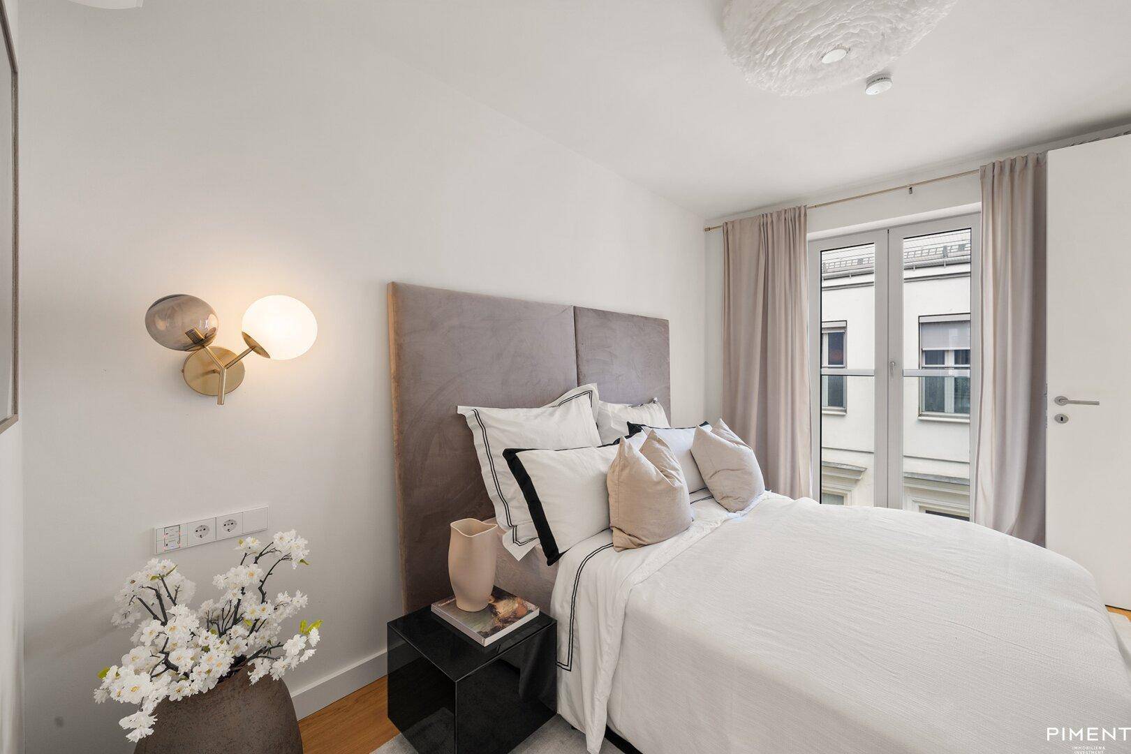 Gemütliches Schlafzimmer mit modernem Bett, Nachttisch und Fenster mit Blick nach draußen.