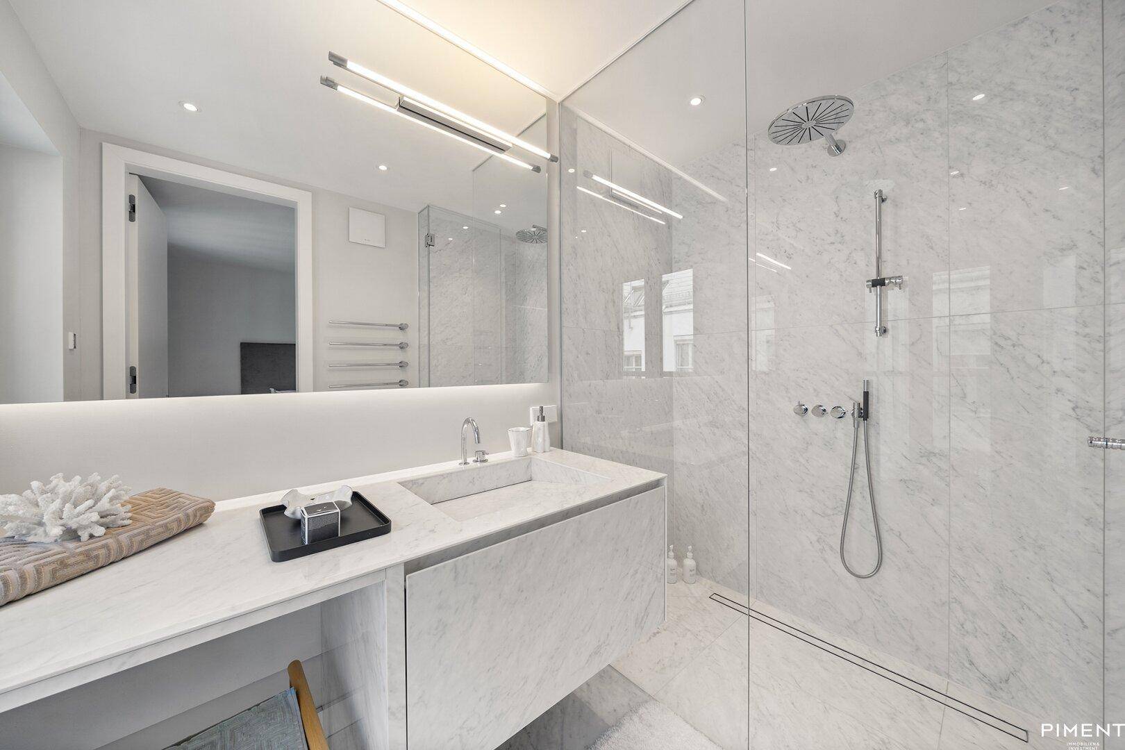 Elegantes Badezimmer mit Marmorfliesen, modernem Waschtisch und einer geräumigen begehbaren Dusche.