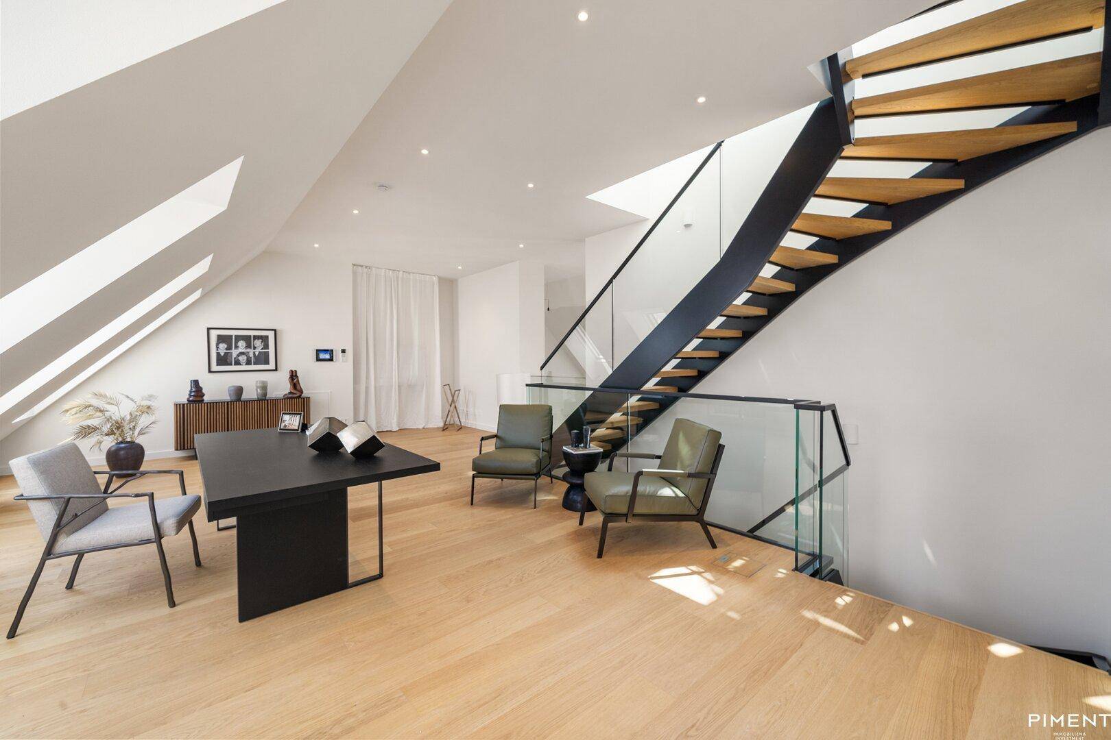 Offener Galeriebereich mit moderner Treppe, Sitzgelegenheiten und schrägen Decken mit Fenstern.