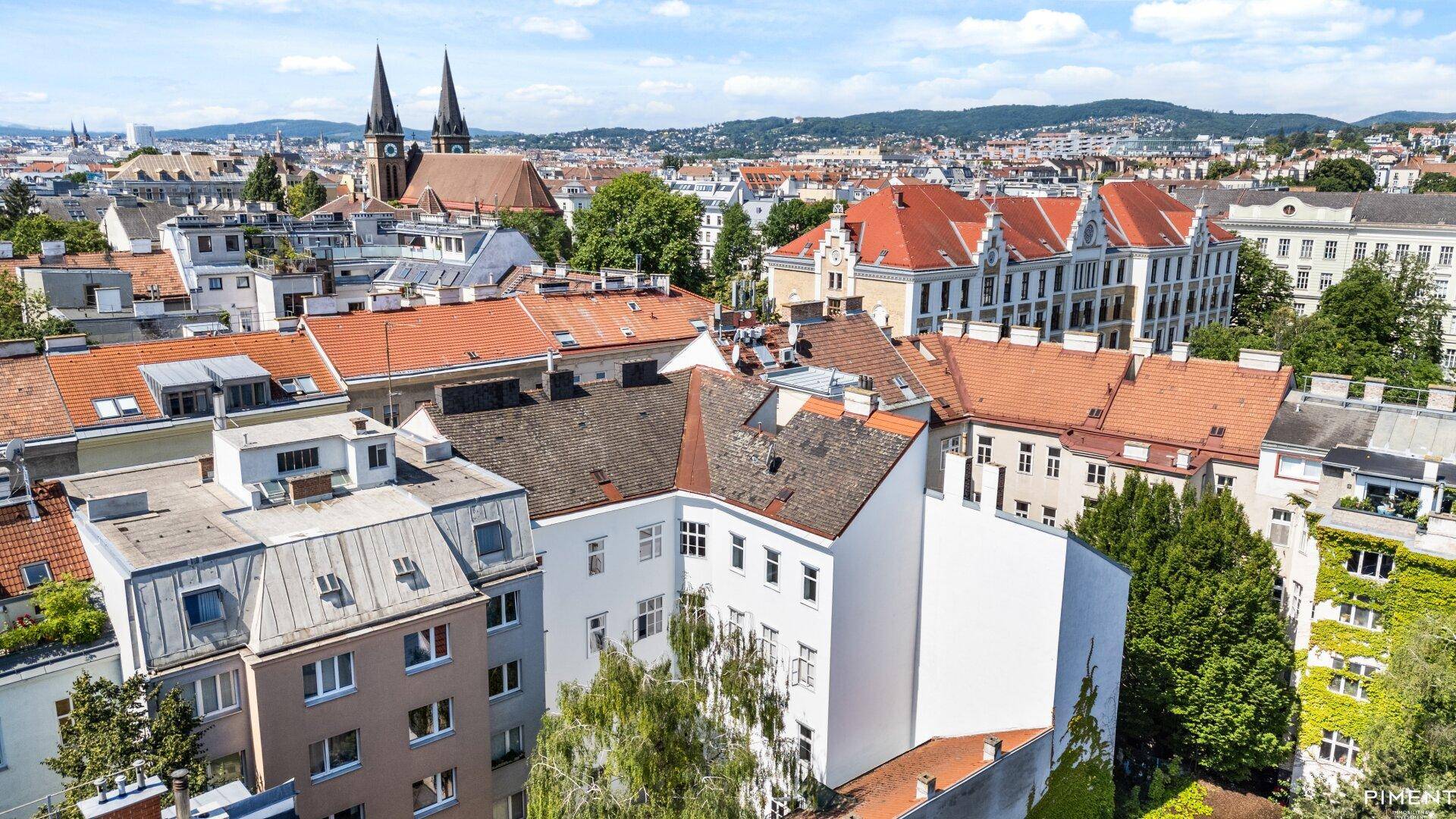 Luftaufnahme eines historischen Stadtviertels mit traditionellen Dächern und einer Kirche im Hintergrund.