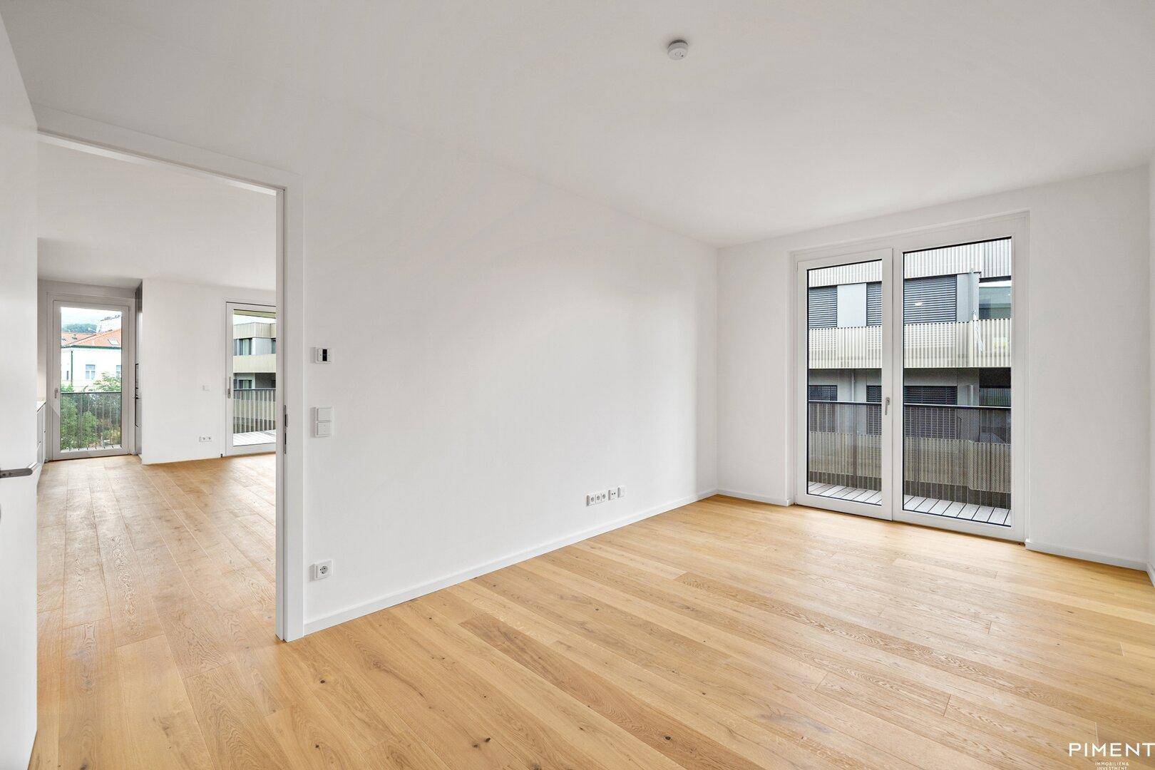 Heller, leerer Raum mit Eichenparkettboden und Zugang zu einem Balkon, ideal für Wohn- oder Schlafzimmer.