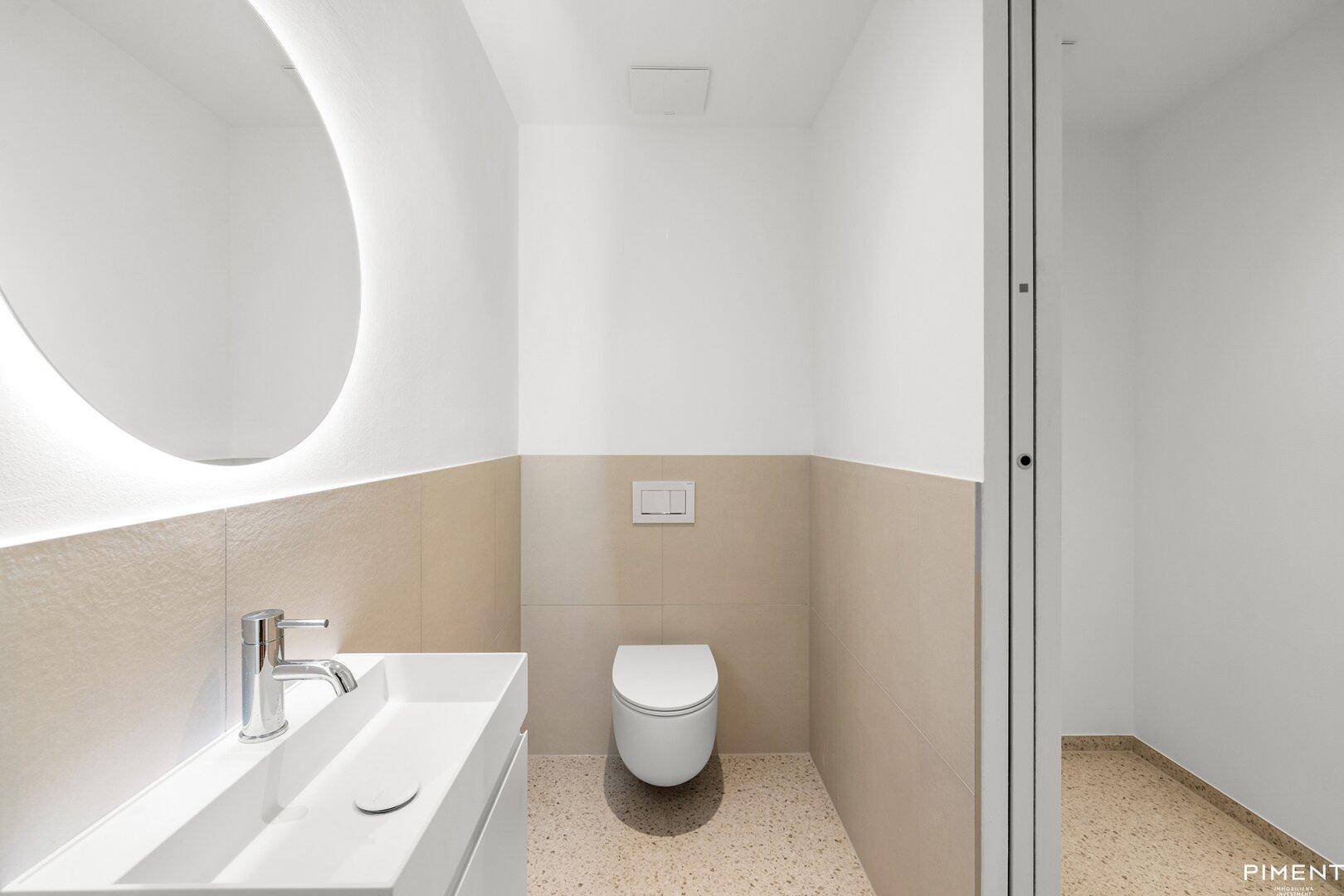 Modernes Gäste-WC mit wandhängender Toilette, Einzelwaschbecken und beleuchtetem Spiegel.