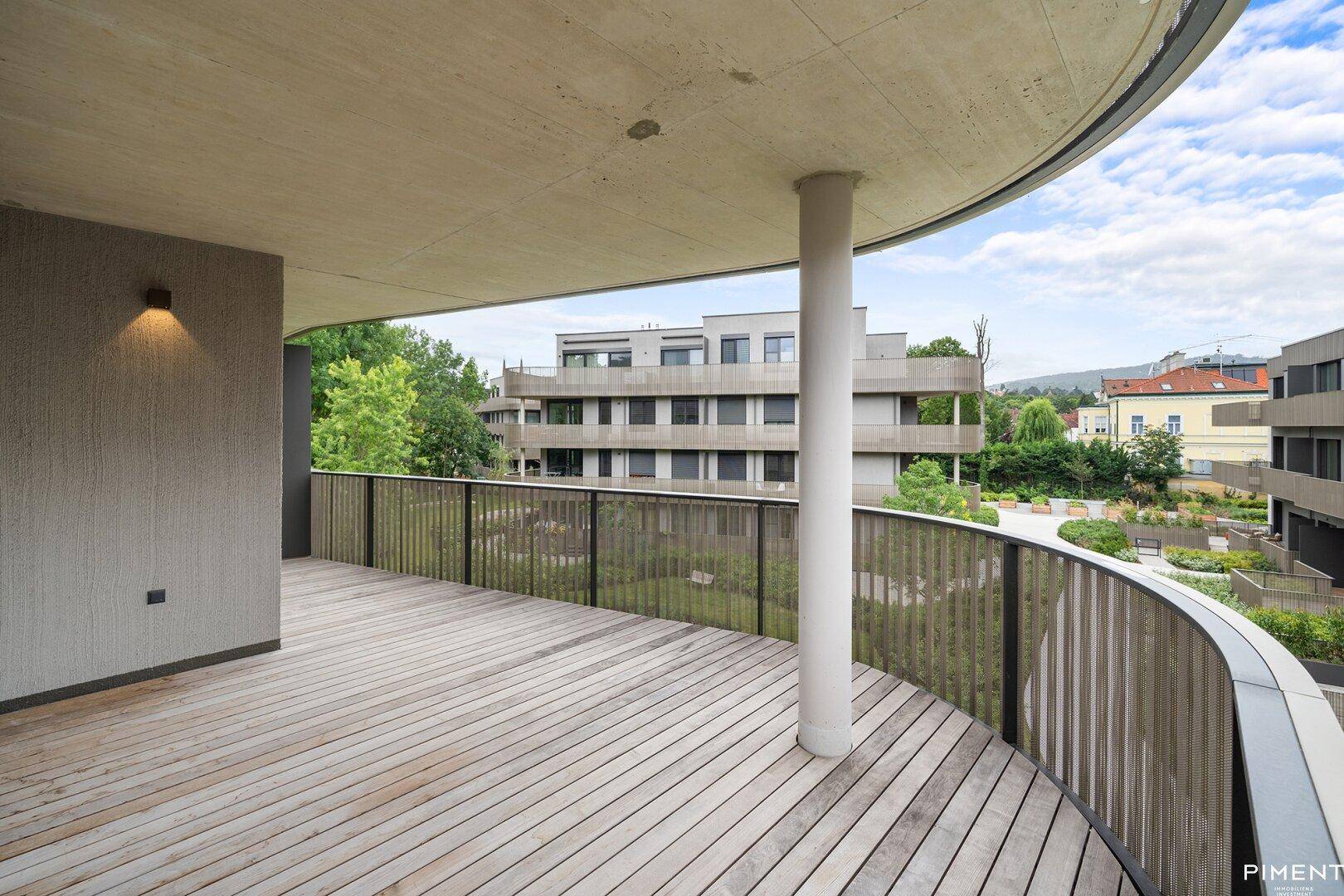 Großer, geschwungener Balkon mit Holzbelag und Blick auf die umliegende moderne Architektur und Grünflächen.