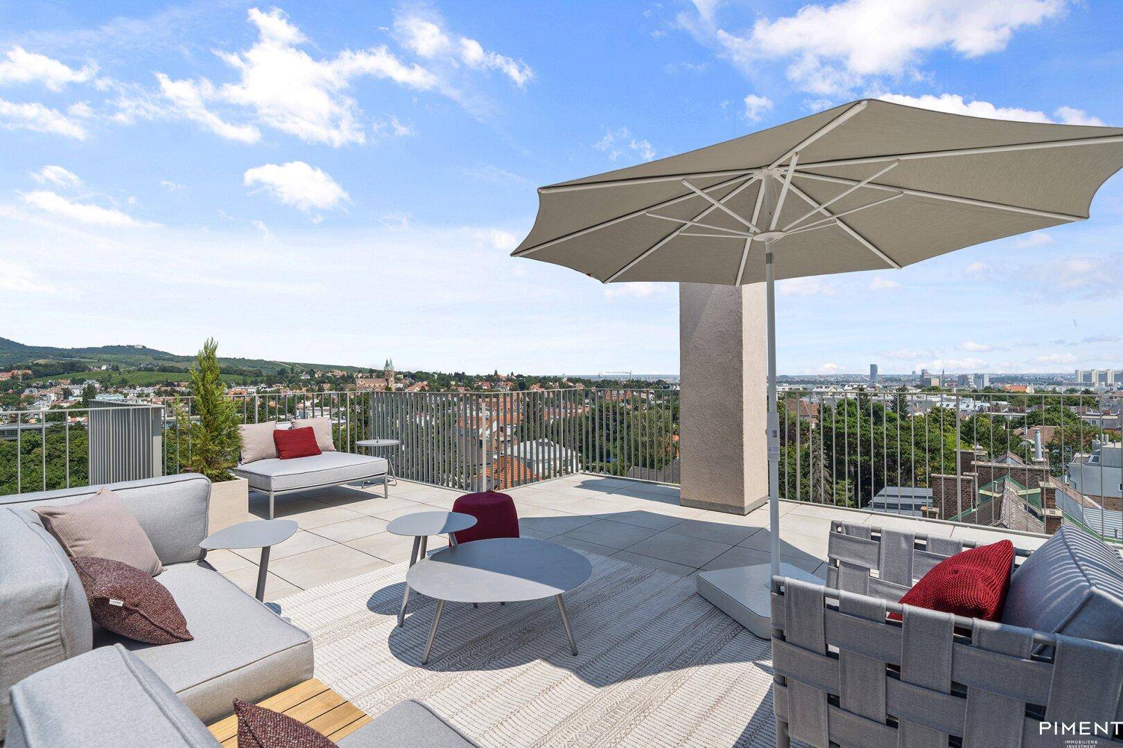 Helle Dachterrasse mit Sonnenschirm, bequemen Sitzgelegenheiten und Panoramablick auf die umliegende Landschaft.