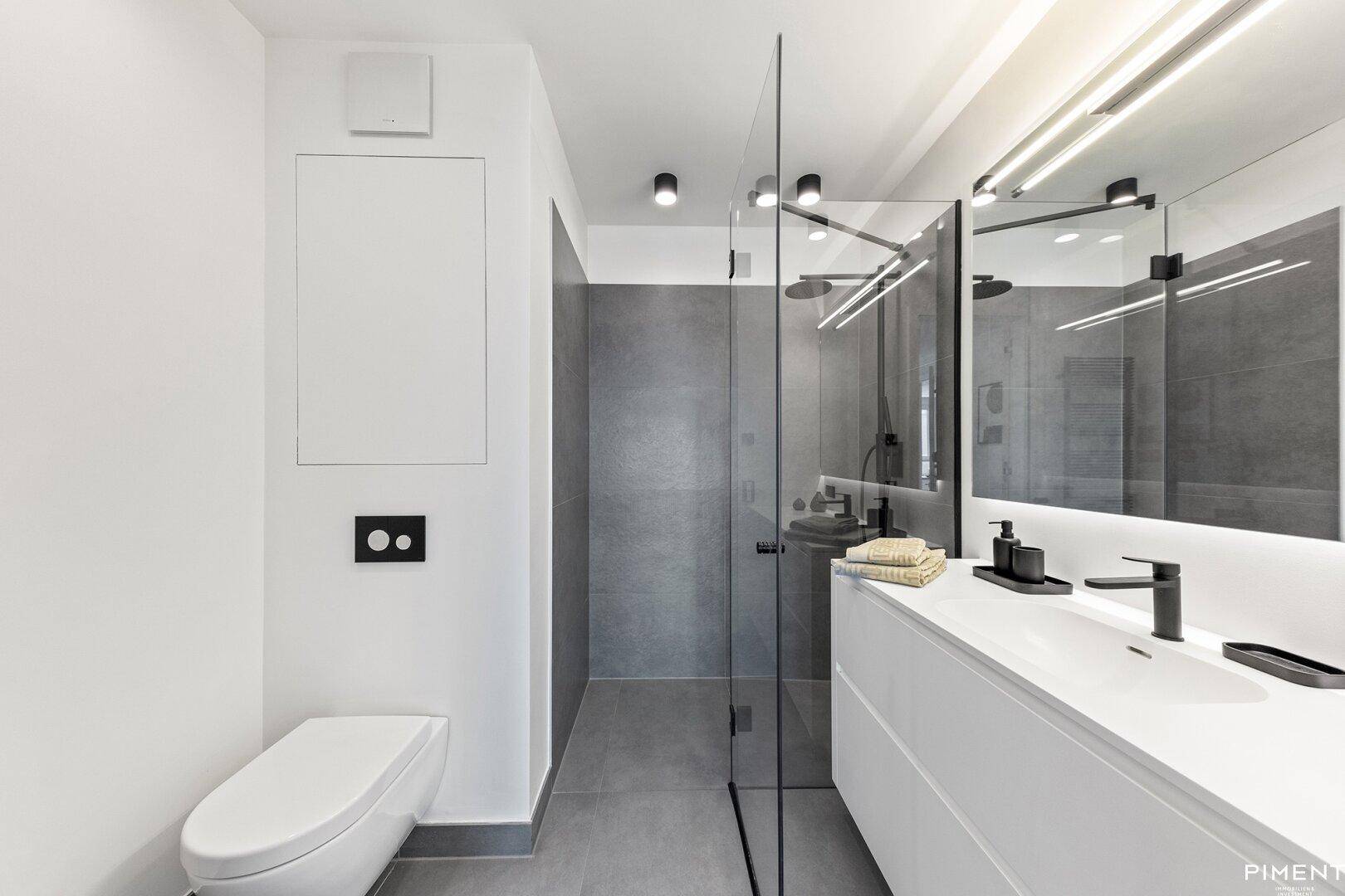 Modernes Badezimmer mit grauen Fliesen, begehbarer Dusche und wandmontierter Toilette.