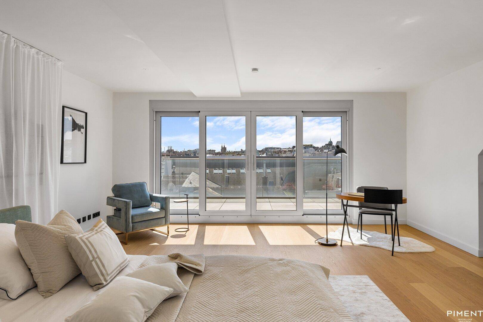 Komfortables Schlafzimmer mit Holzboden, großen Fenstern und Blick auf die Stadt.