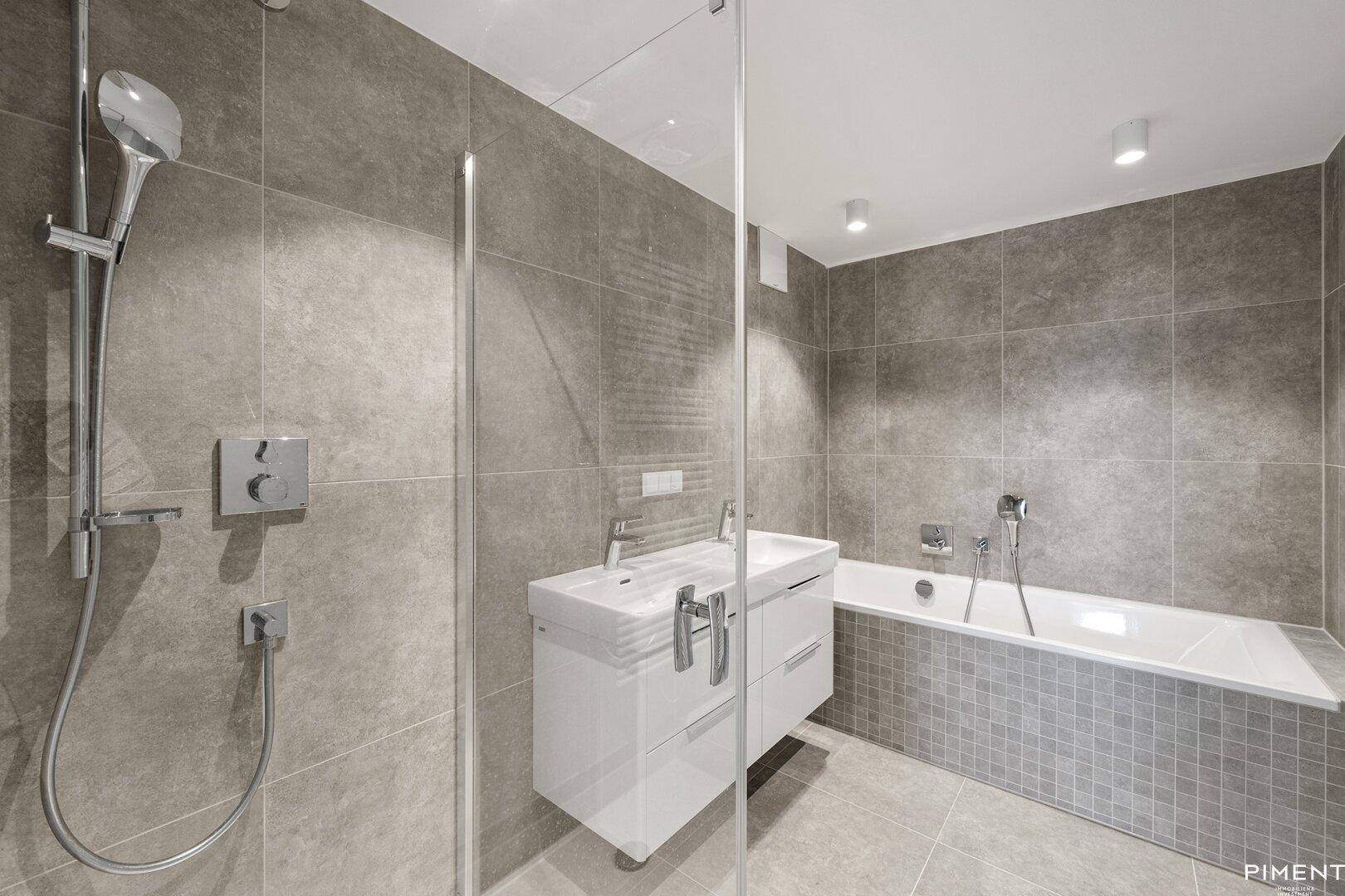 Modernes Badezimmer mit grauen Fliesen, Badewanne und separater Dusche.