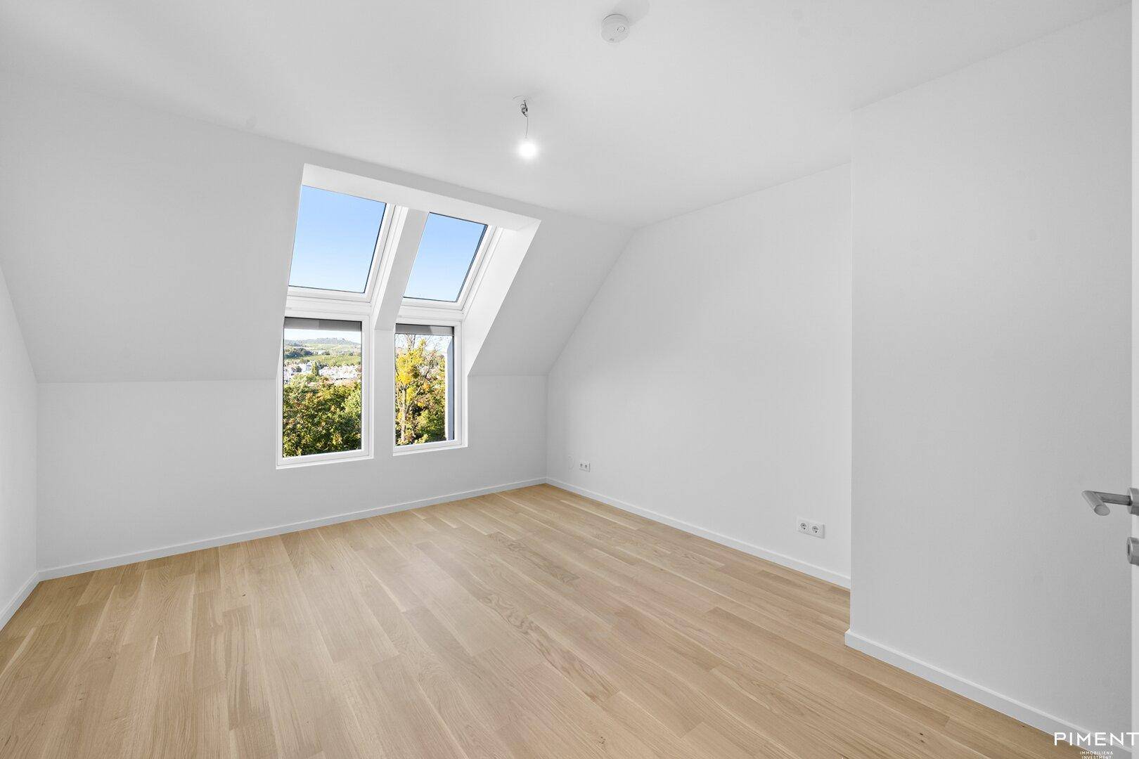 Schlafzimmer im Dachgeschoss mit Holzboden, Dachfenstern und Blick ins Grüne.