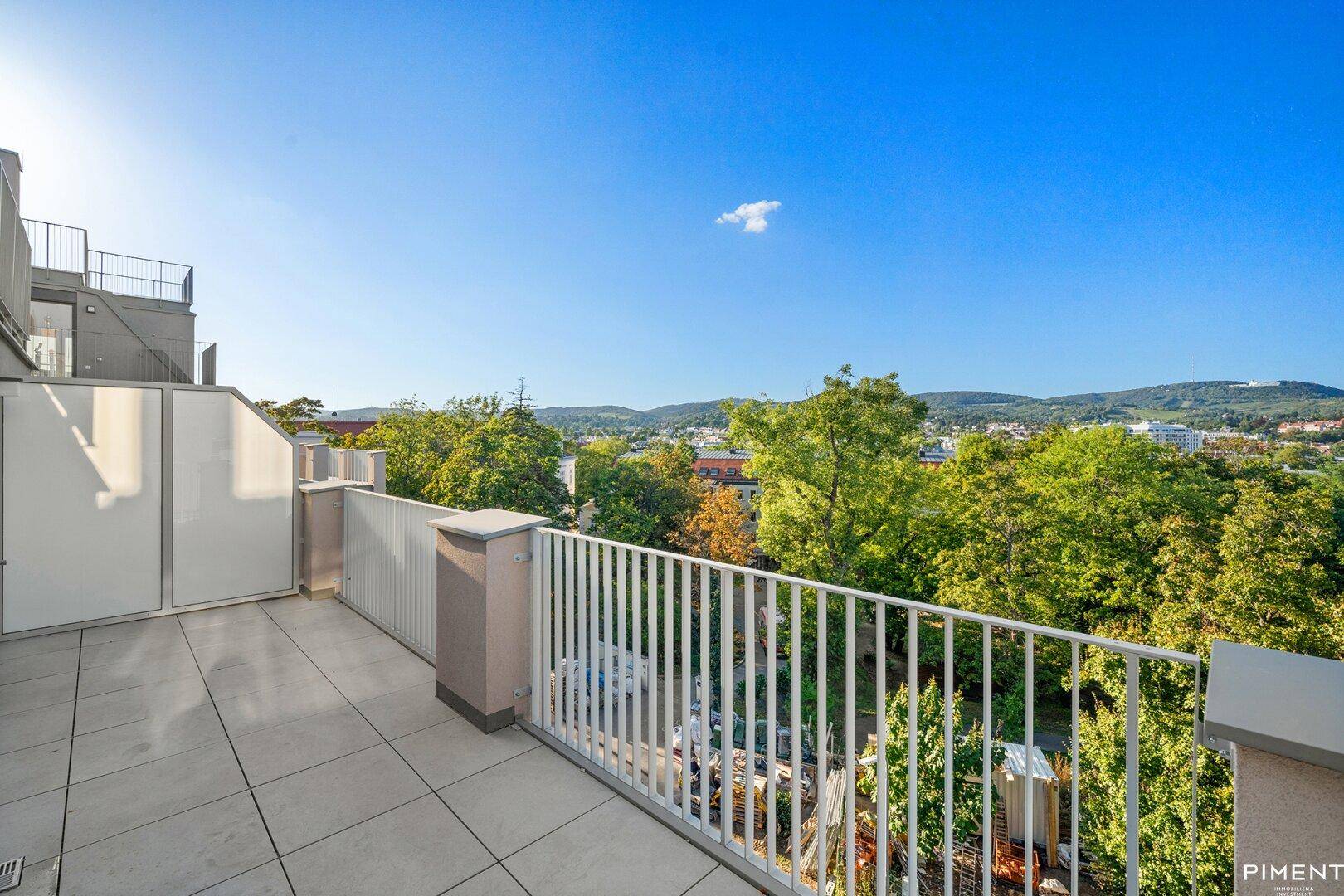Sonnige Terrasse mit Fliesenboden und weitem Blick über die grüne Umgebung.