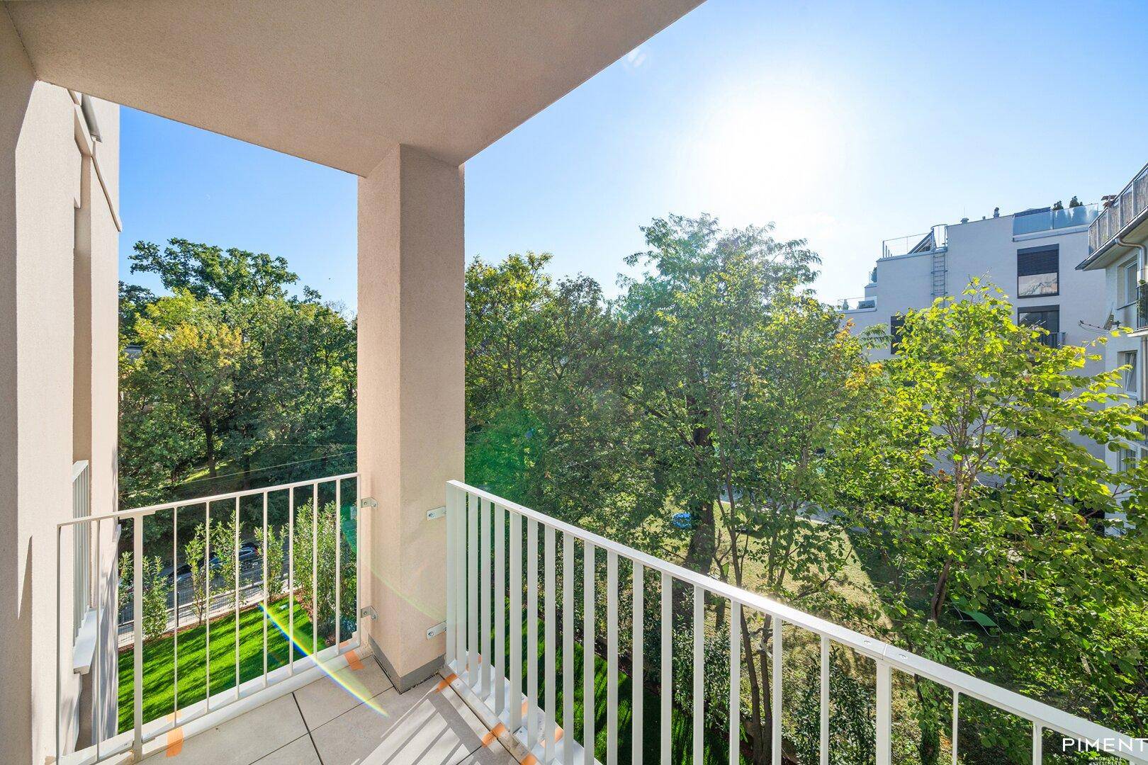 Sonniger Balkon mit Blick ins Grüne und auf die umliegenden Gebäude.