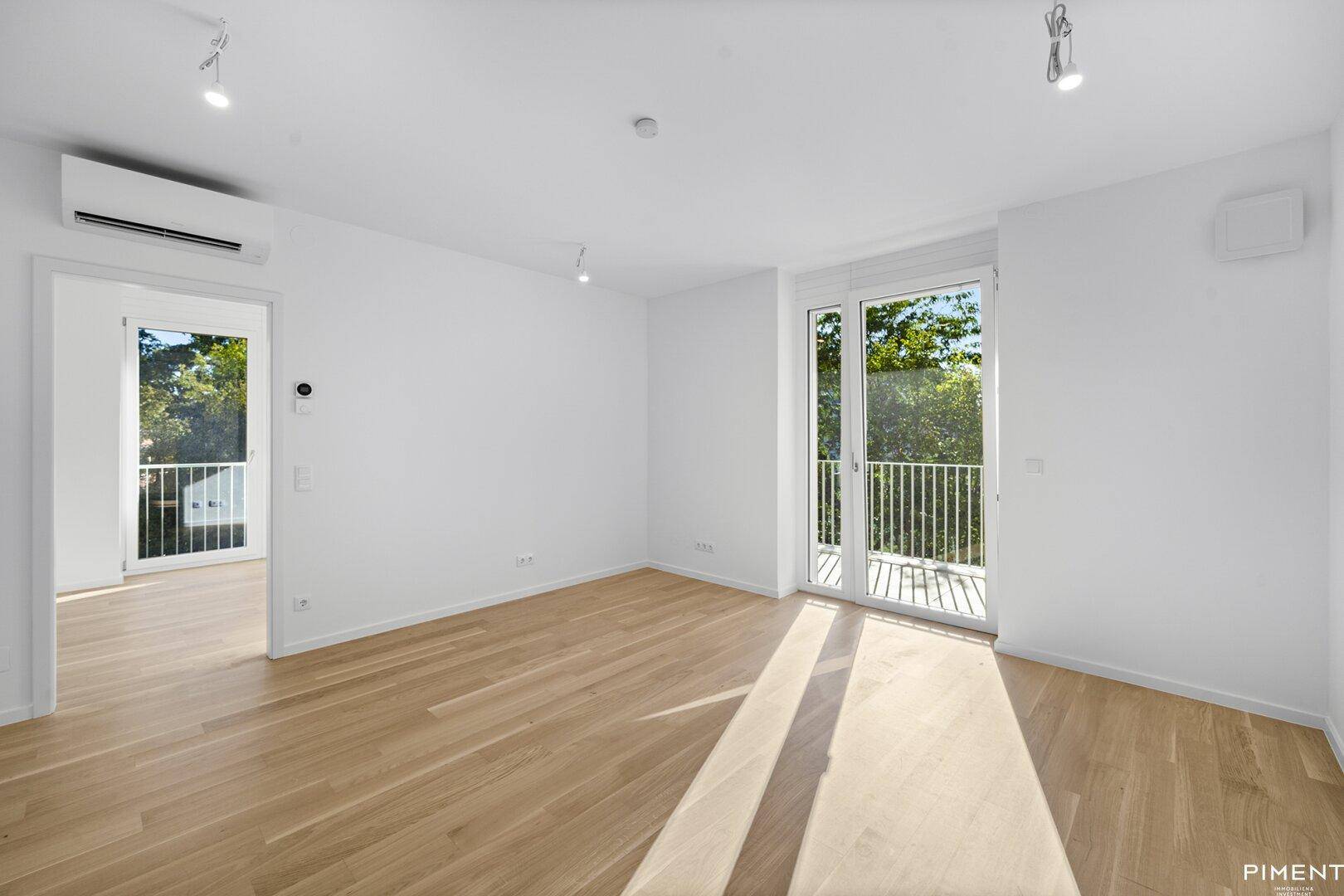 Geräumiges, helles Zimmer mit Holzboden, Klimaanlage und Zugang zu einem französischen Balkon.