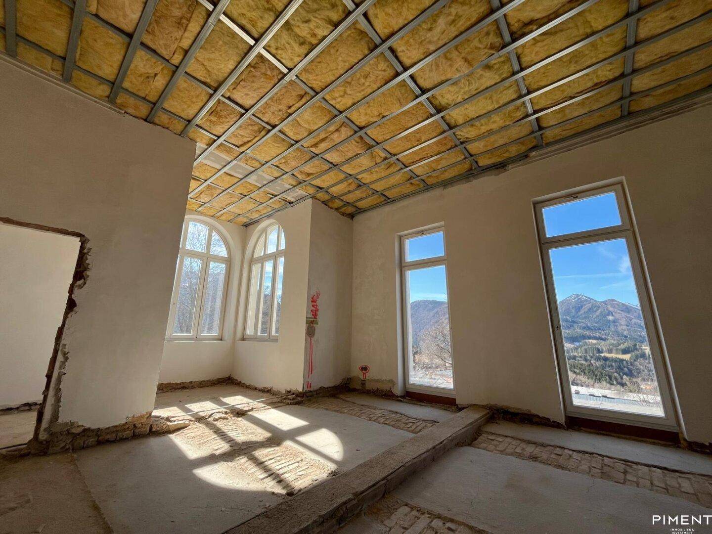 Geräumiger Innenraum im Rohbau mit großen Fenstern und weitem Bergblick.