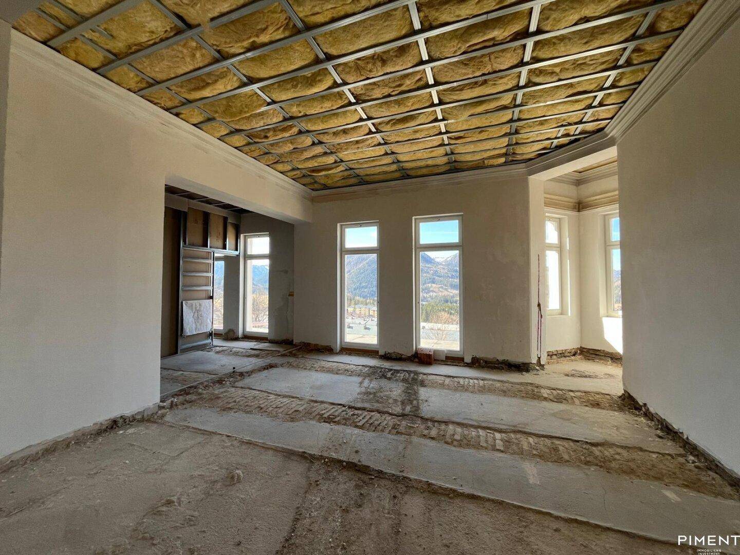 Großer Raum im Rohbau mit hohen Decken und weitem Blick auf die Berglandschaft.