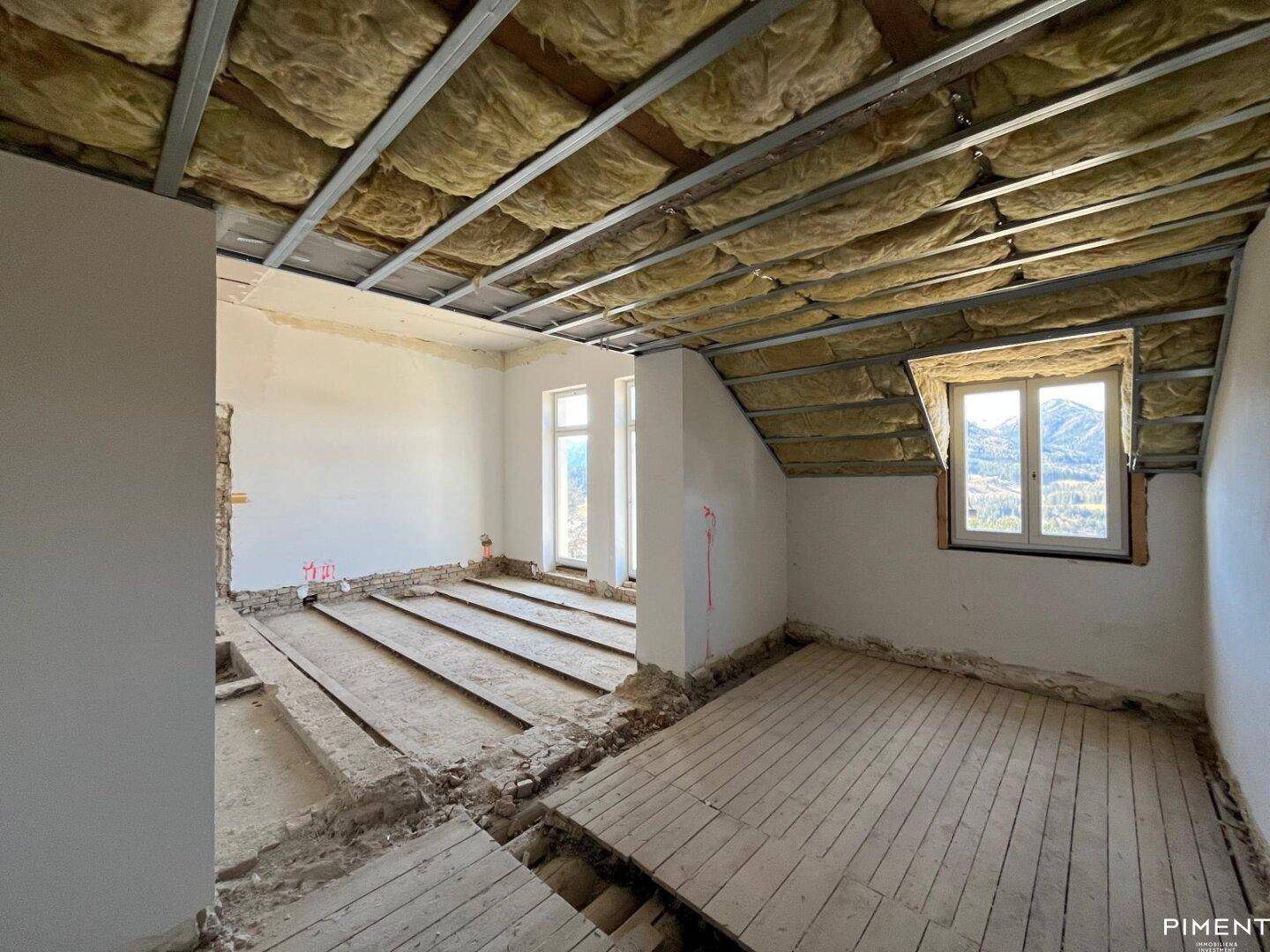 Dachgeschoss im Rohbau mit Holzboden und schrägen Decken, bereit für den Ausbau.