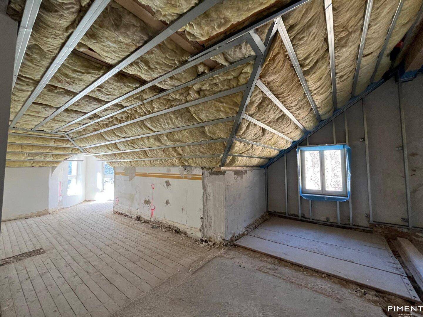 Geräumiges Dachgeschoss im Rohbau mit sichtbarer Dachkonstruktion und Fenstern.