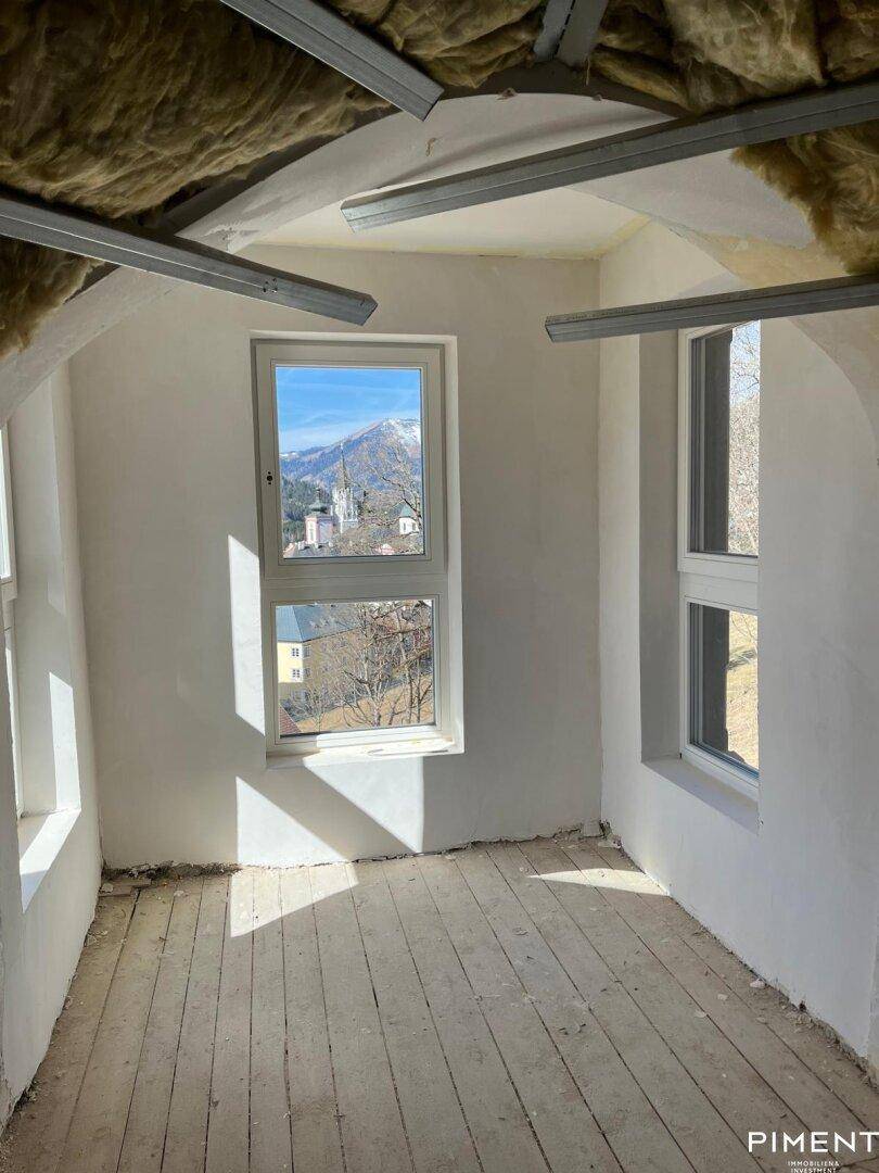 Helles Dachgeschosszimmer im Rohbau mit Holzboden und Bergblick.