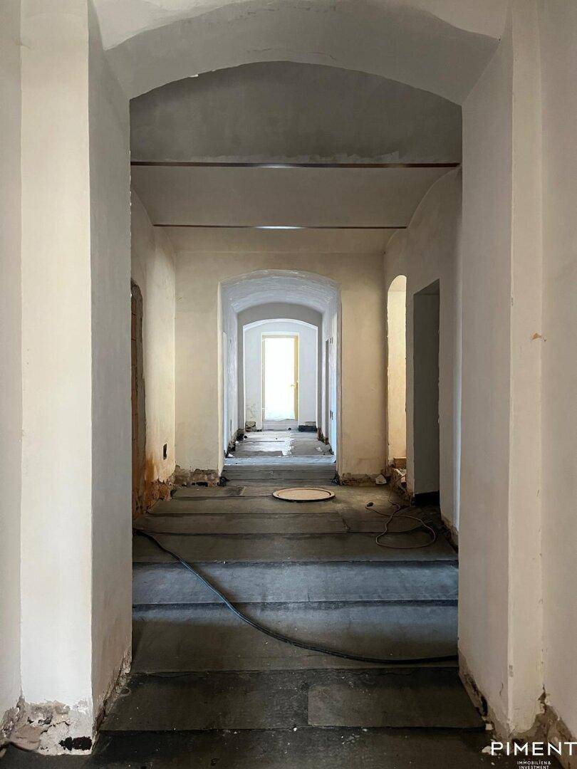 Langer, gewölbter Flur im Rohbau mit natürlichem Lichteinfall am Ende.