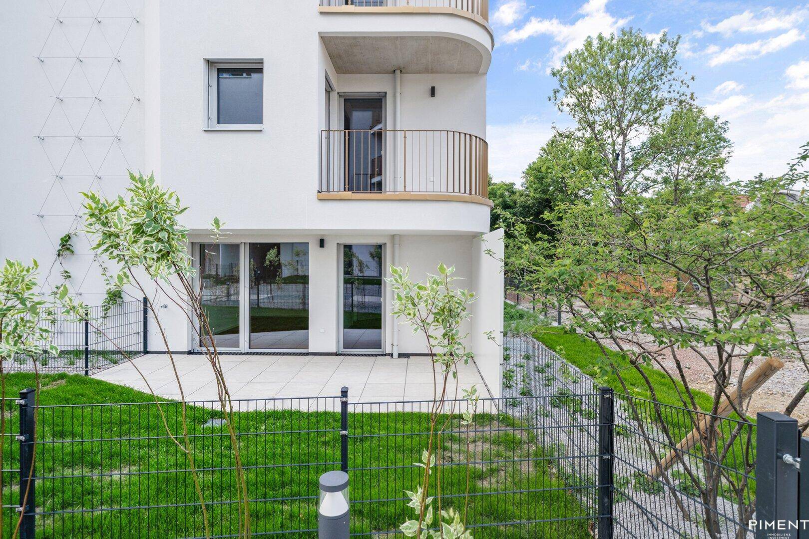 Ebenerdige Terrasse mit kleinem Rasenbereich und Zugang zu einem modernen Wohngebäude.
