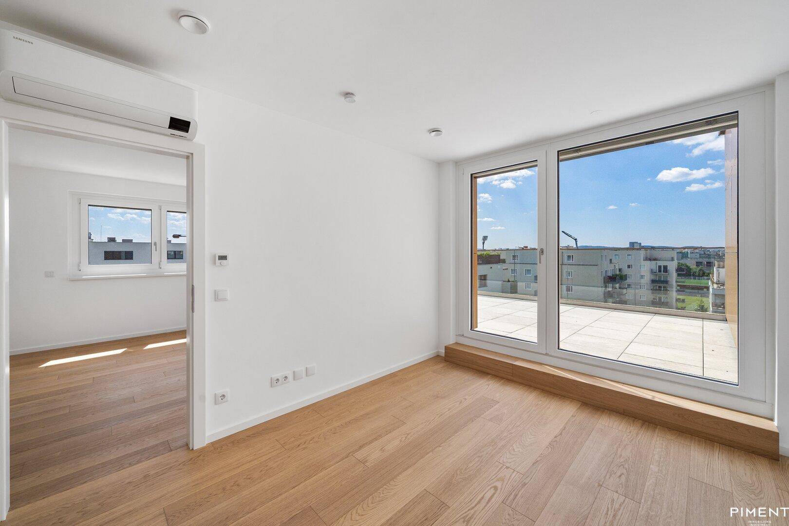 Geräumiger, heller Raum mit Holzboden, Klimaanlage und großem Fenster mit direktem Terrassenzugang.