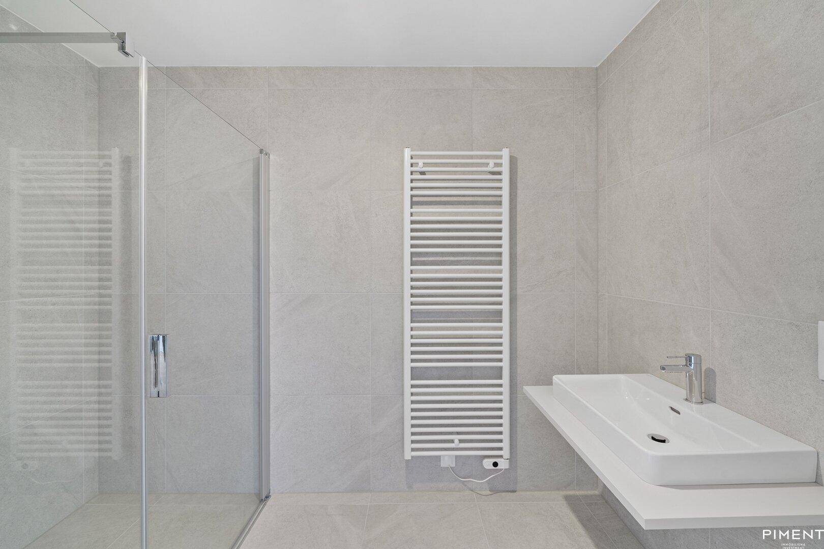 Modernes Badezimmer mit grauen Fliesen, ebenerdiger Dusche, Einzelwaschbecken und beheiztem Handtuchhalter.