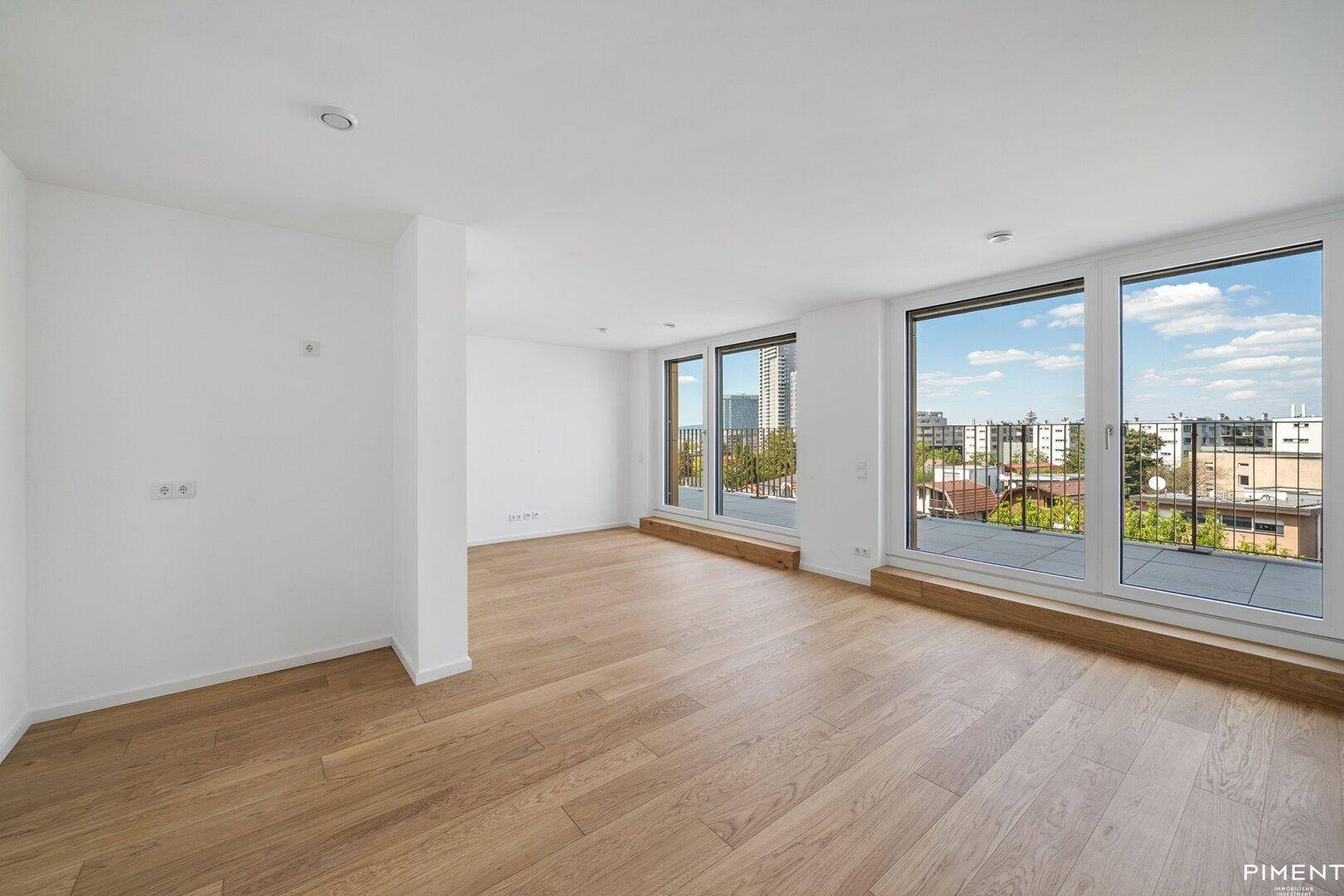 Geräumiger, heller Raum mit Holzboden und großen Fenstern, die viel Tageslicht hereinlassen.