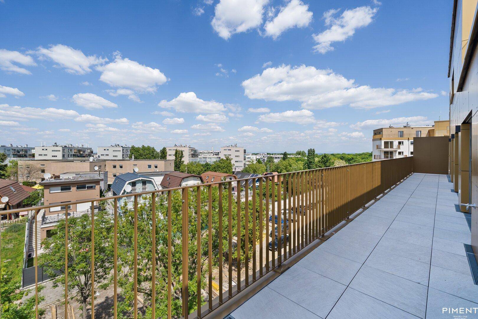 Lange, schmale Terrasse mit moderner Brüstung und Blick auf die umliegenden Gebäude und Grünflächen.