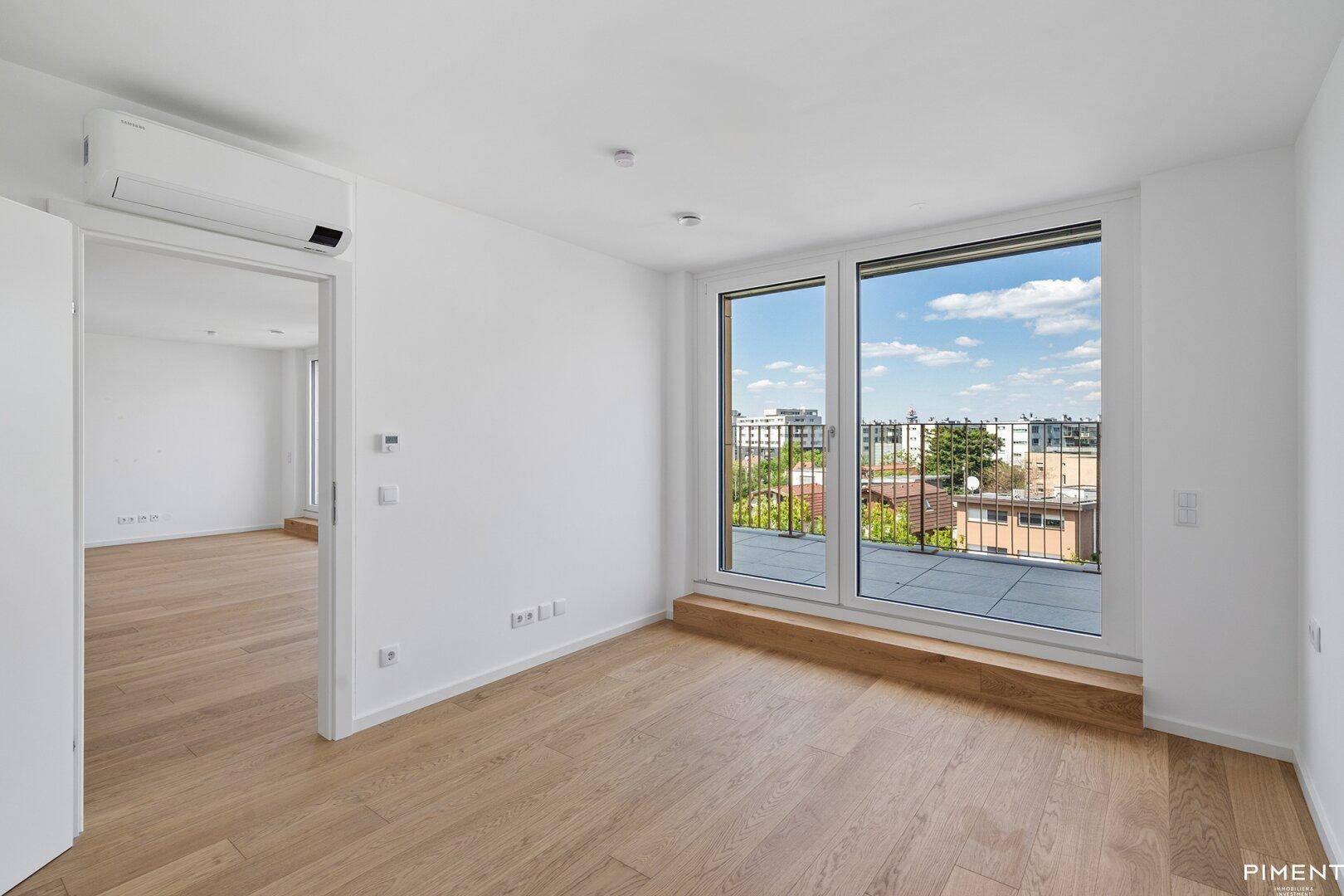 Helles Zimmer mit Holzboden, Klimaanlage und Zugang zu einem Außenbereich mit schöner Aussicht.