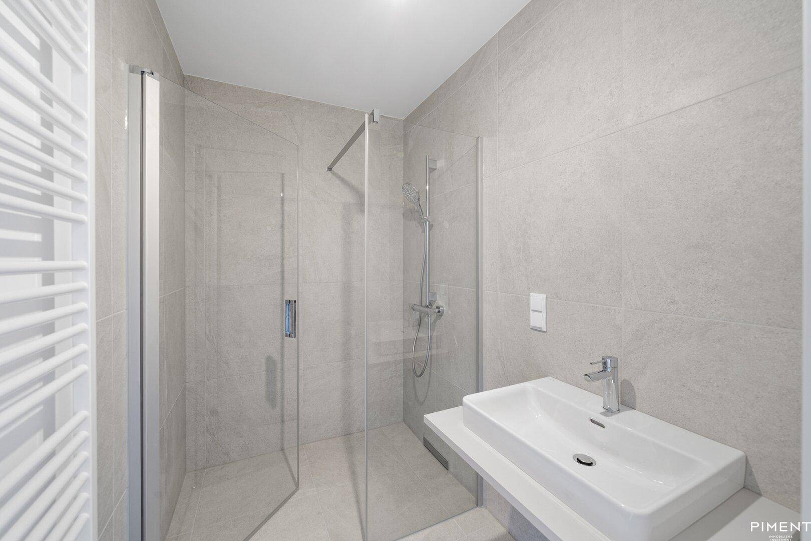 Modernes Badezimmer mit grauen Fliesen, ebenerdiger Dusche und einem stilvollen Einzelwaschbecken.