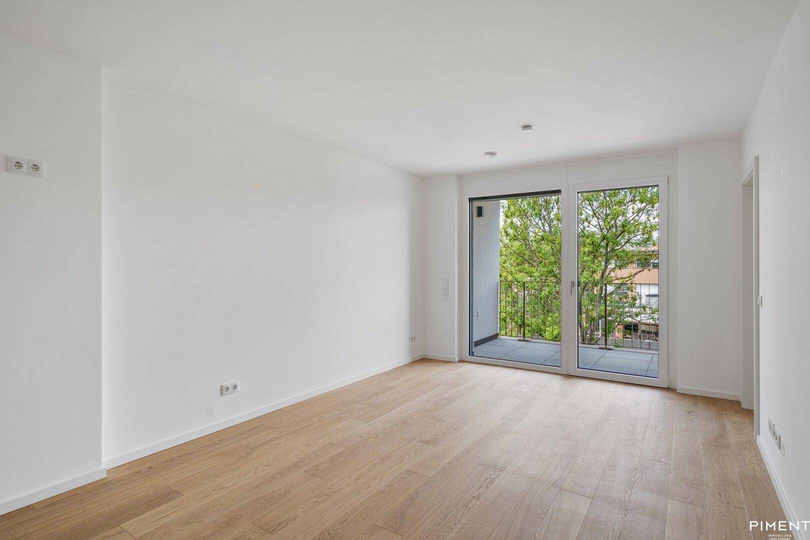 Heller Wohnraum mit Parkettboden und Zugang zu einem Balkon mit Blick ins Grüne.
