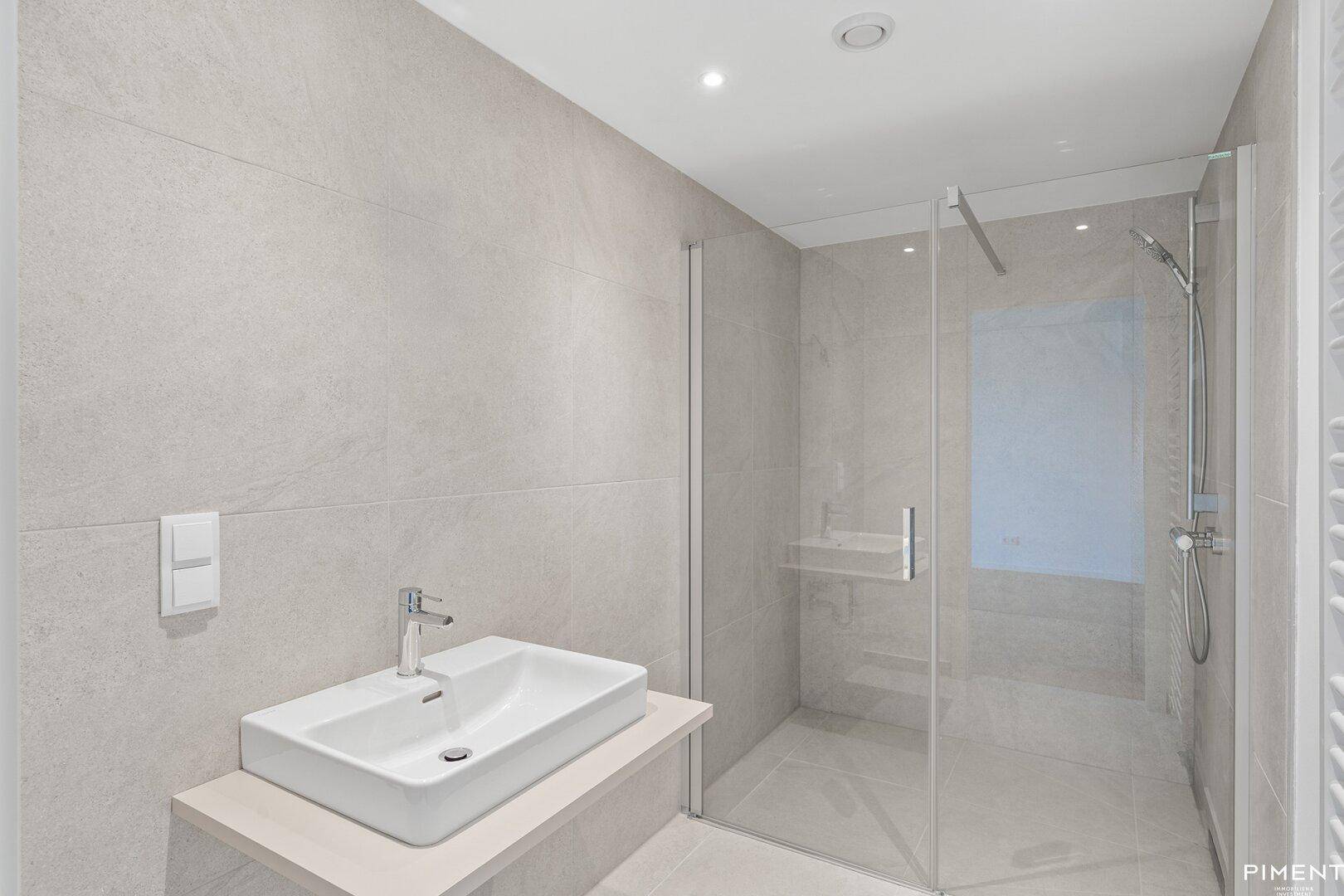 Modernes Badezimmer mit begehbarer Dusche, großformatigen Fliesen und Einzelwaschbecken.