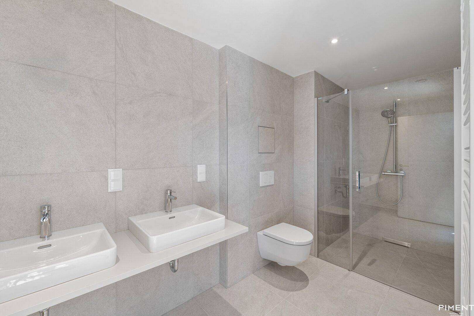 Modernes Badezimmer mit hellgrauen Fliesen, Doppelwaschbecken und einer geräumigen begehbaren Dusche.