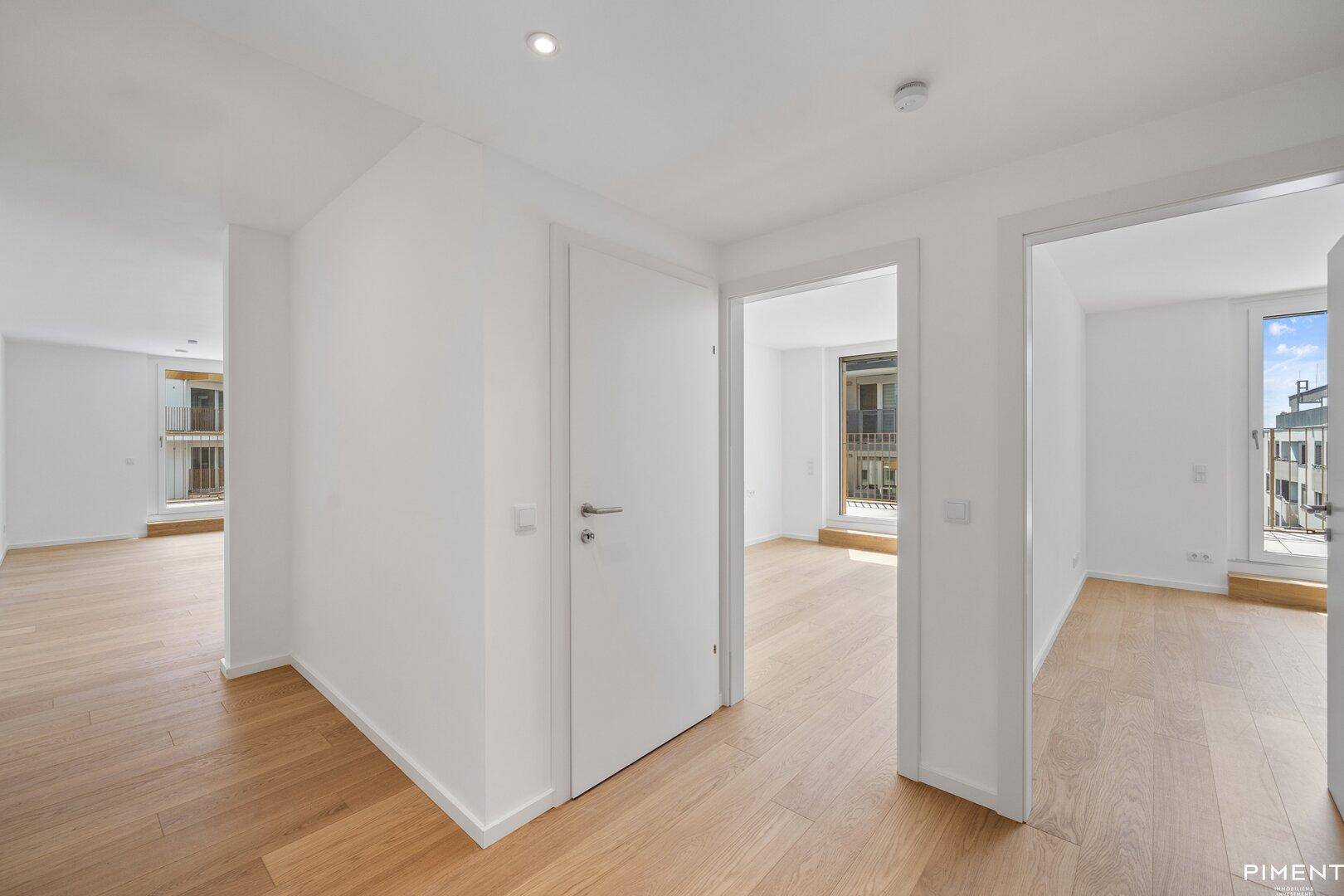 Heller Flur mit Holzboden und mehreren Türen, der zu verschiedenen Räumen und einem Balkon führt.