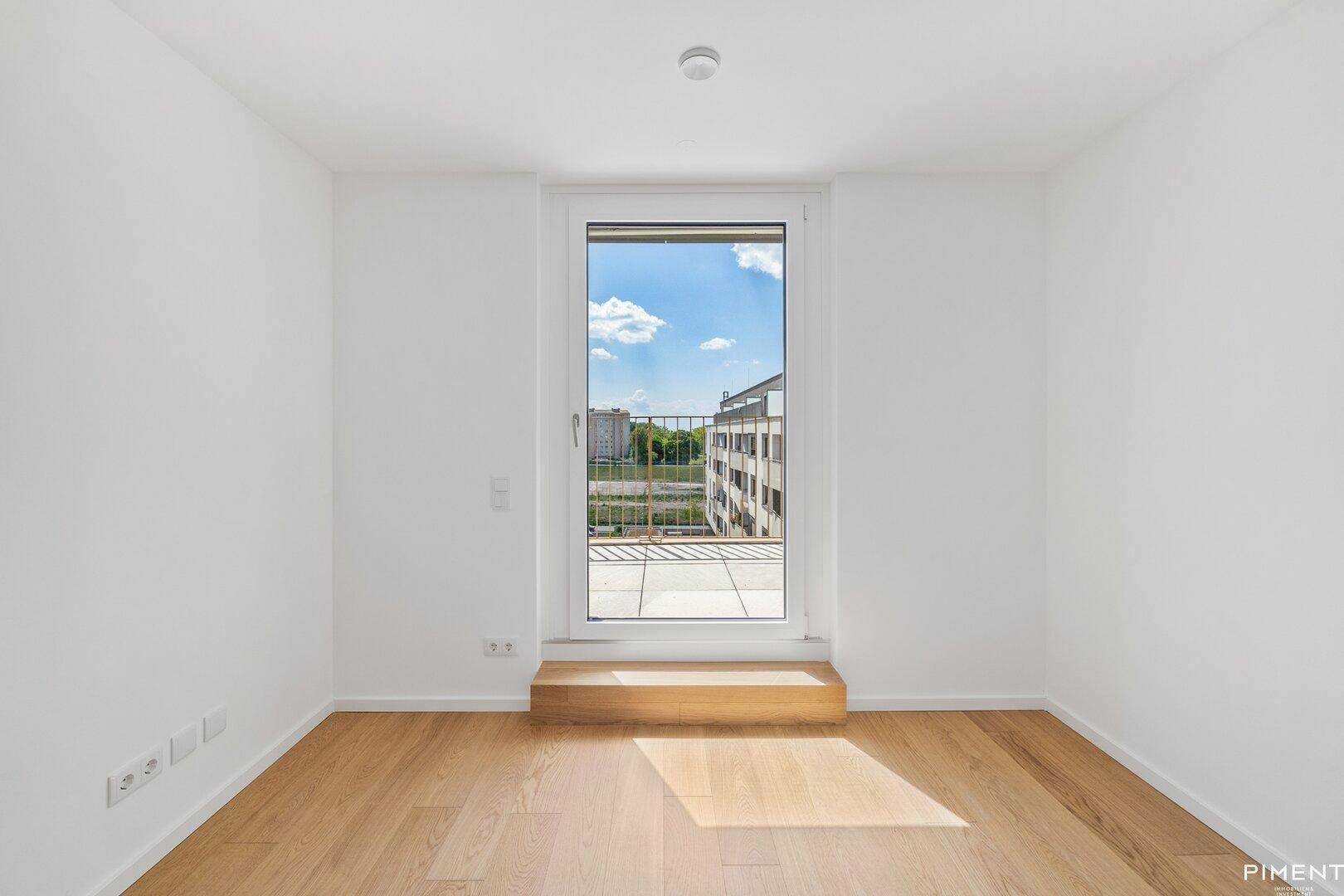 Helles Zimmer mit Holzboden und Zugang zu einem Außenbereich, ideal als Schlafzimmer oder Büro.