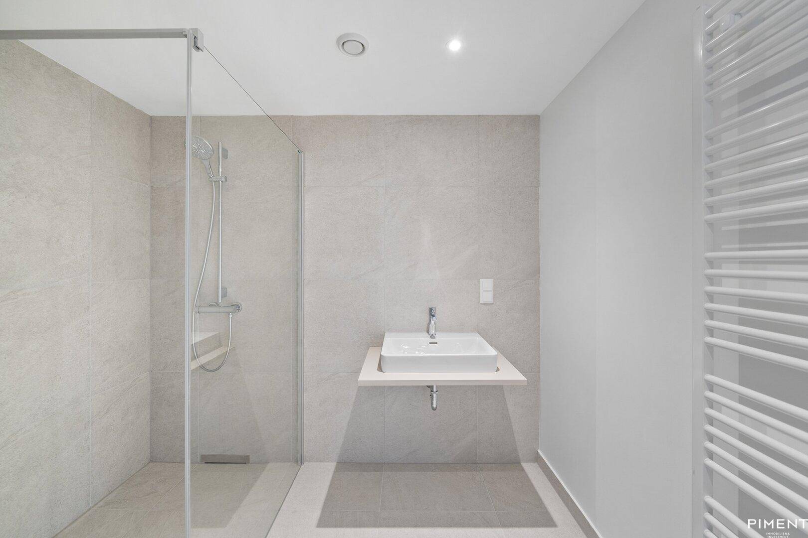 Modernes Badezimmer mit begehbarer Dusche, hellen Fliesen und einem praktischen beheizten Handtuchhalter.