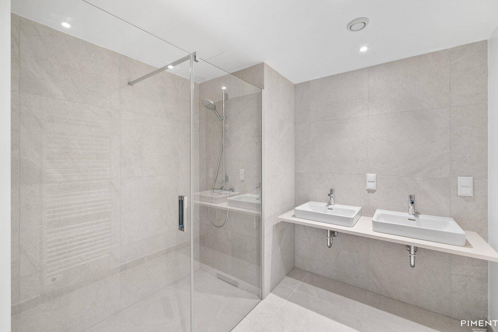 Modernes Badezimmer mit Doppelwaschbecken, großer begehbarer Dusche und hellen Fliesen.