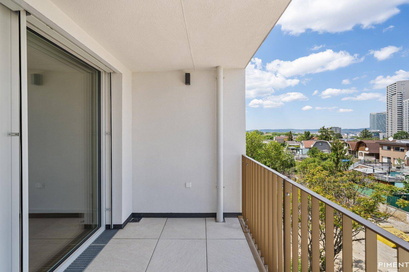 Heller Balkon mit Fliesenboden und weitem Blick über die Stadt und grüne Umgebung.