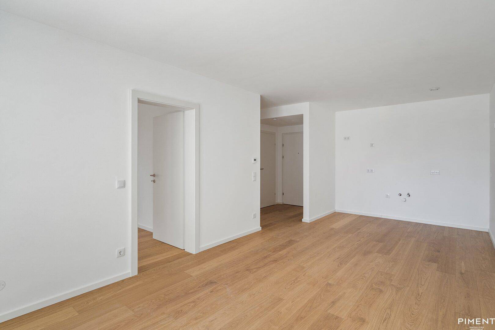 Heller Innenraum mit Eichenparkett und weißen Wänden, der mehrere offene Durchgänge zeigt.