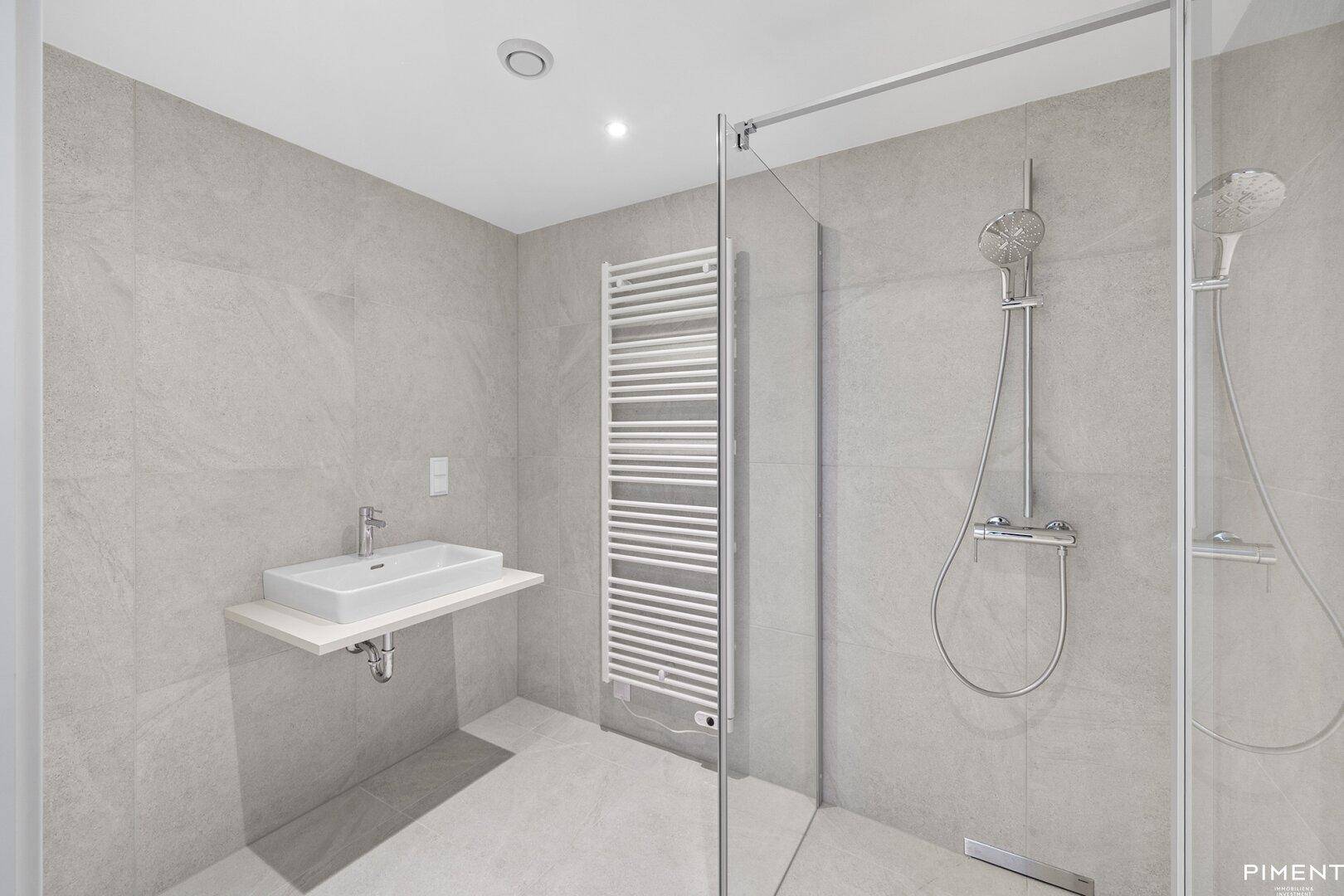 Modernes Badezimmer mit grauen Fliesen, ebenerdiger Dusche und beheiztem Handtuchhalter.